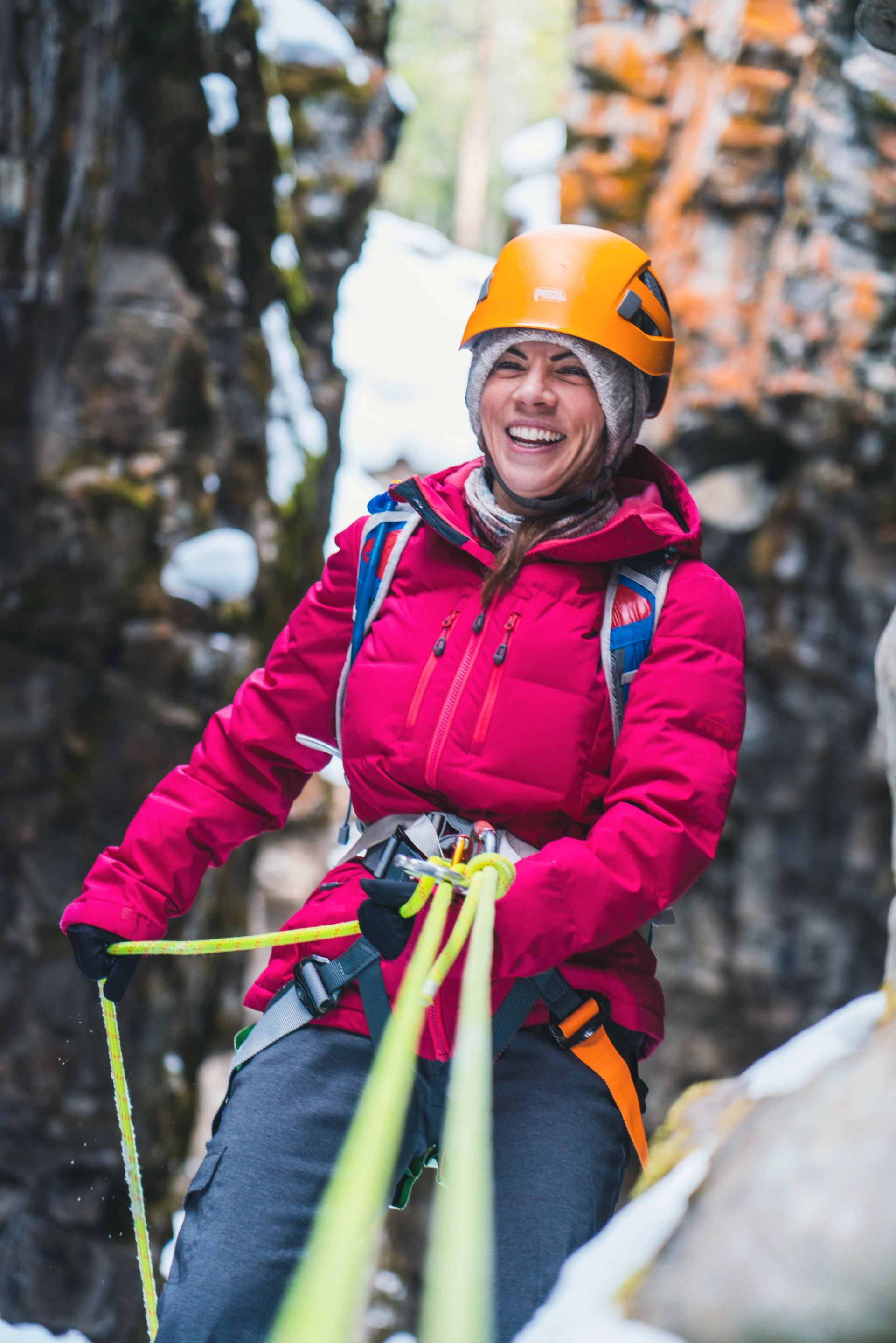 Participant in red jacket rappelling down a snowy canyon using bright yellow ropes.