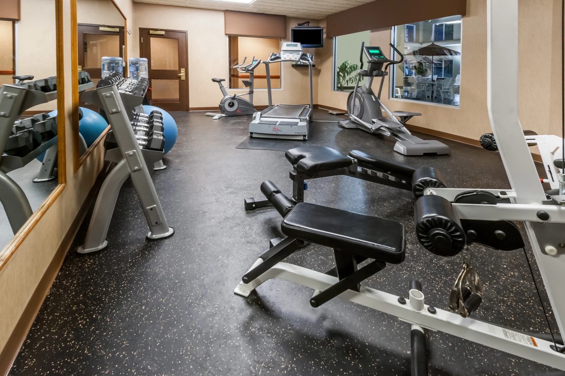 Fitness room with exercise machines, weight bench, treadmill, and stationary bikes in view.