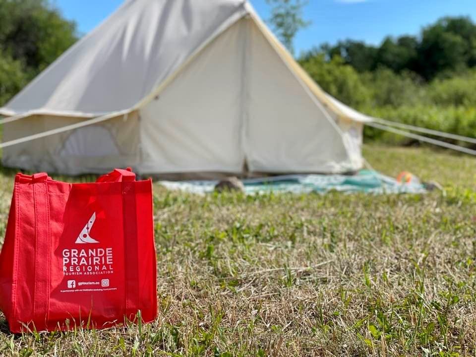 White canvas tent in grassy area with red Grande Prairie tote bag