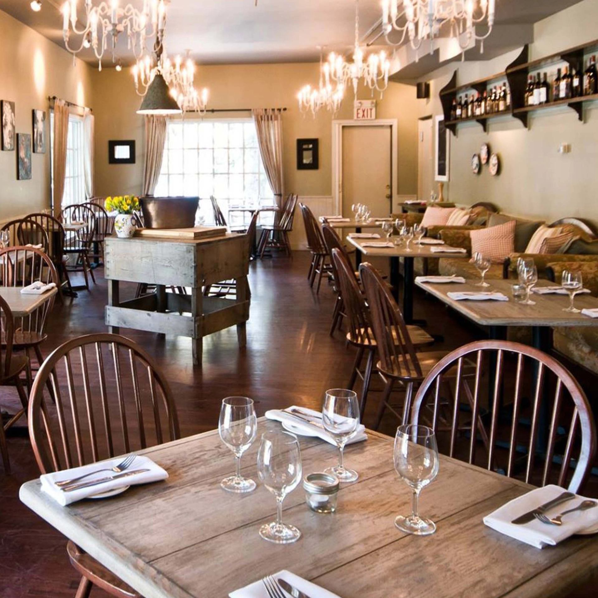 Restaurant dining room with set wooden tables, chairs, chandeliers and cushioned benches.