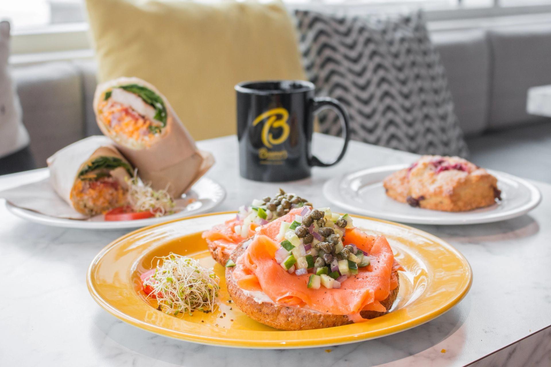 Plate with smoked salmon toast, a wrap, a scone, and a Beamer’s mug on a marble table.