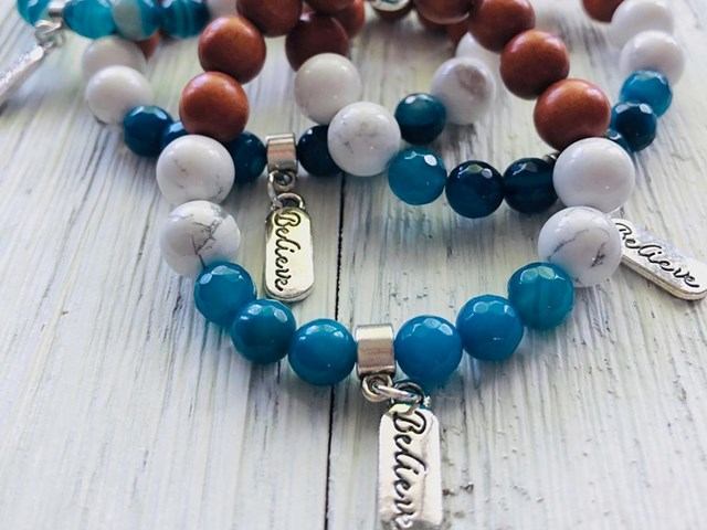 Beaded bracelet with blue, white, and brown beads and metal charm clasps on wood background.