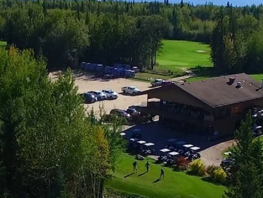 Golf course clubhouse, driving range, parked cars, and players on green at Gilwood Golf and Country .