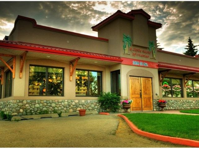 Las Palmeras building with red roof, stone trim, and potted plants at entrance.