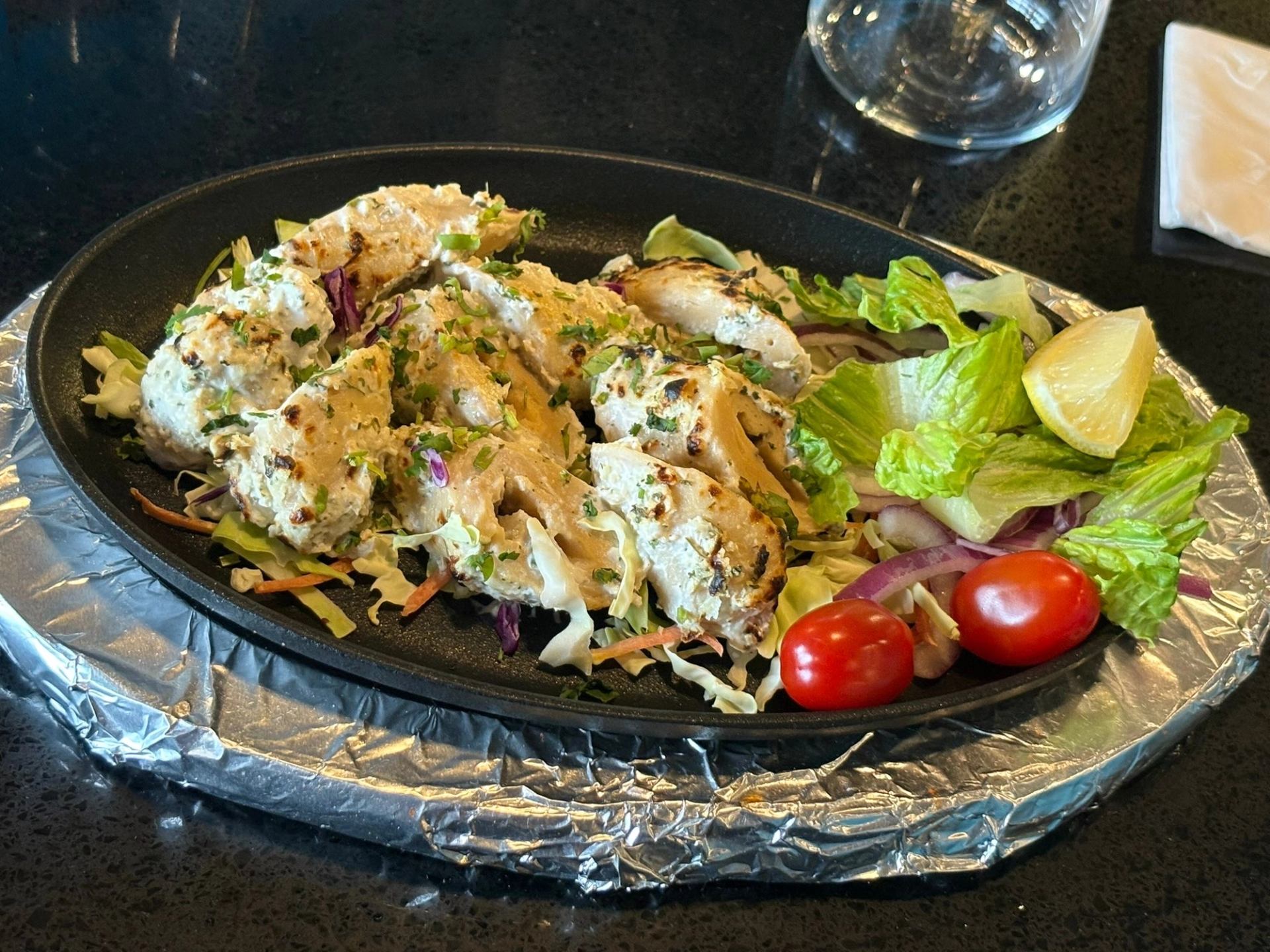 Grilled chicken with herbs, creamy sauce, and salad on a black plate.