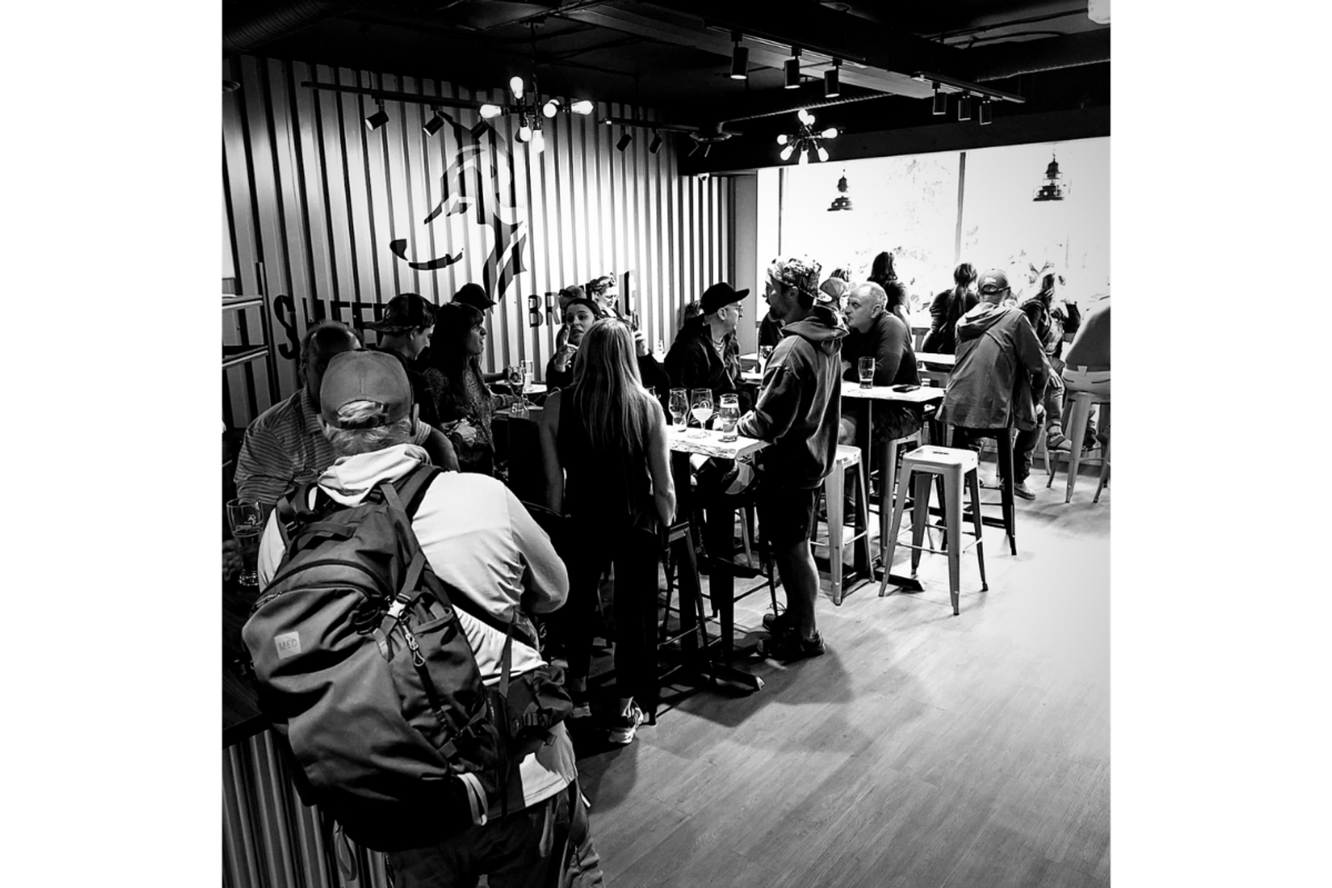 Crowded brewery taproom with patrons gathered around high tables and stools.