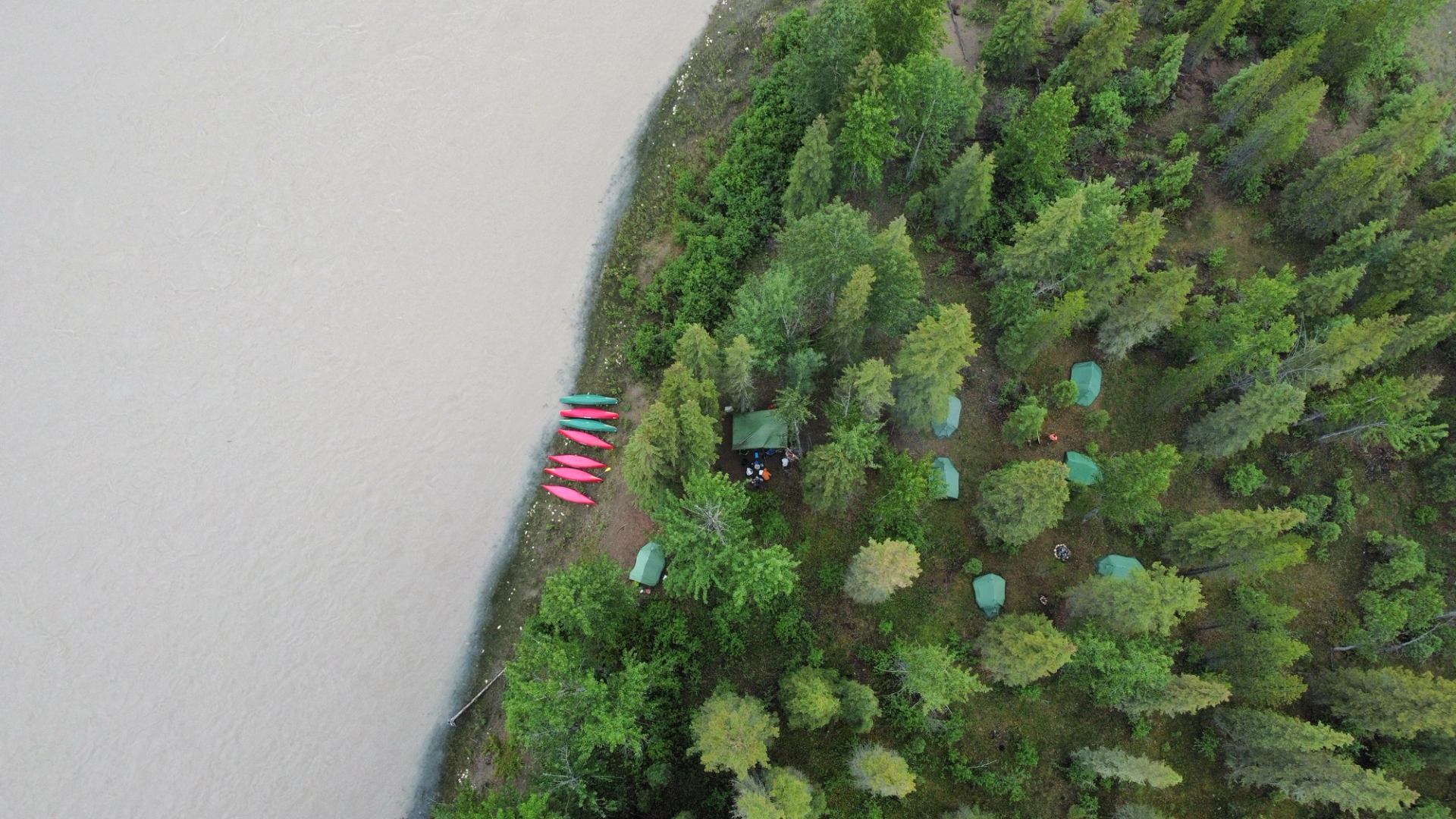 Drone shot of canoes on shore and tents within the forest.