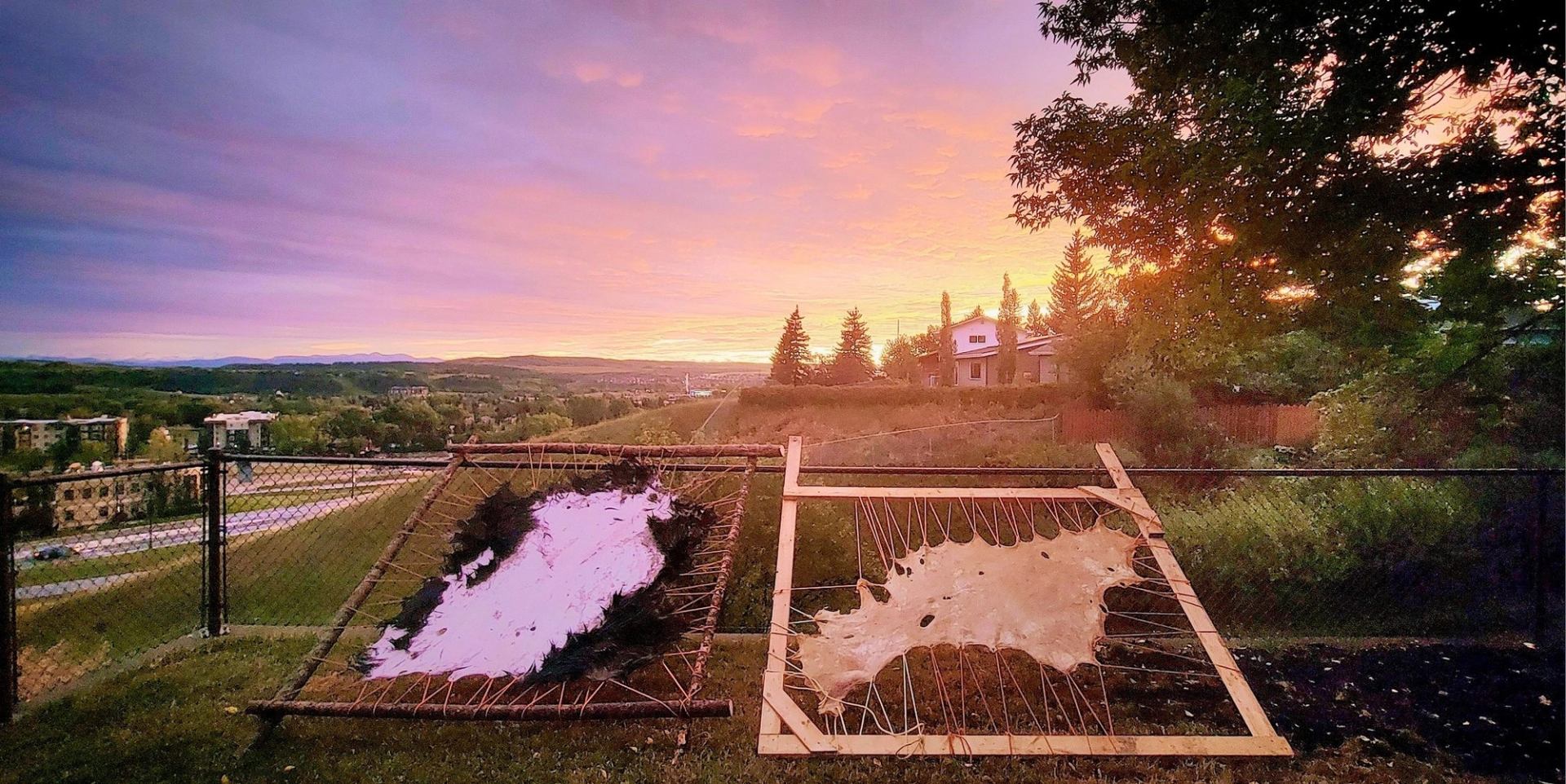 Two animal hides stretched on wooden frames overlooking a valley at sunset.