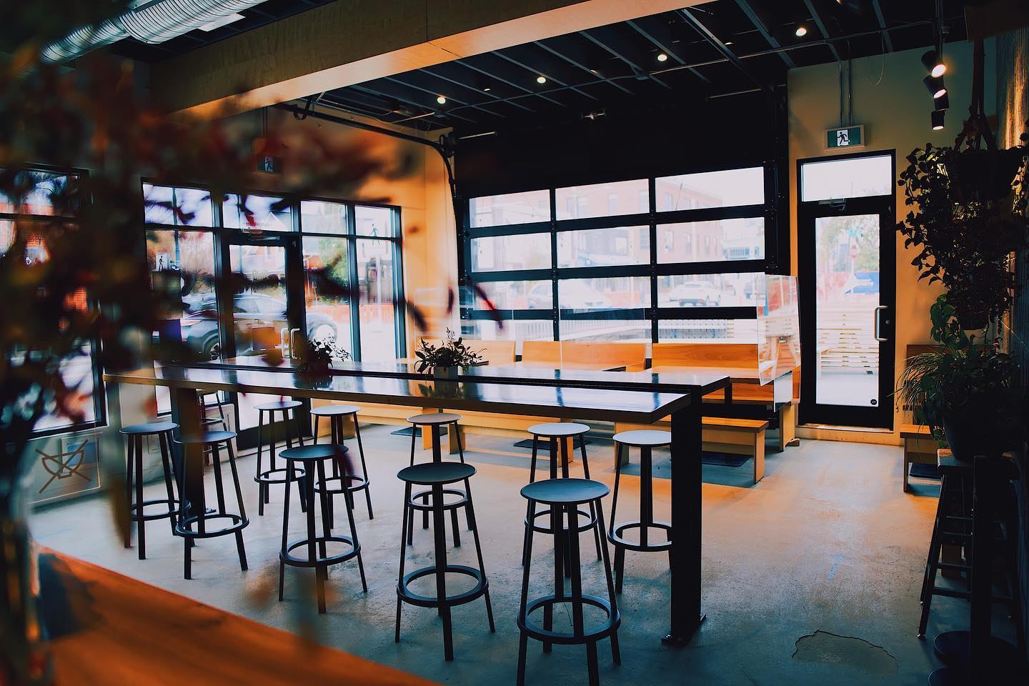 Modern cafe interior with a long table, bar stools, and large glass windows.