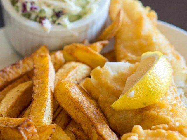 Plate of battered fish and chips with lemon wedge and coleslaw.