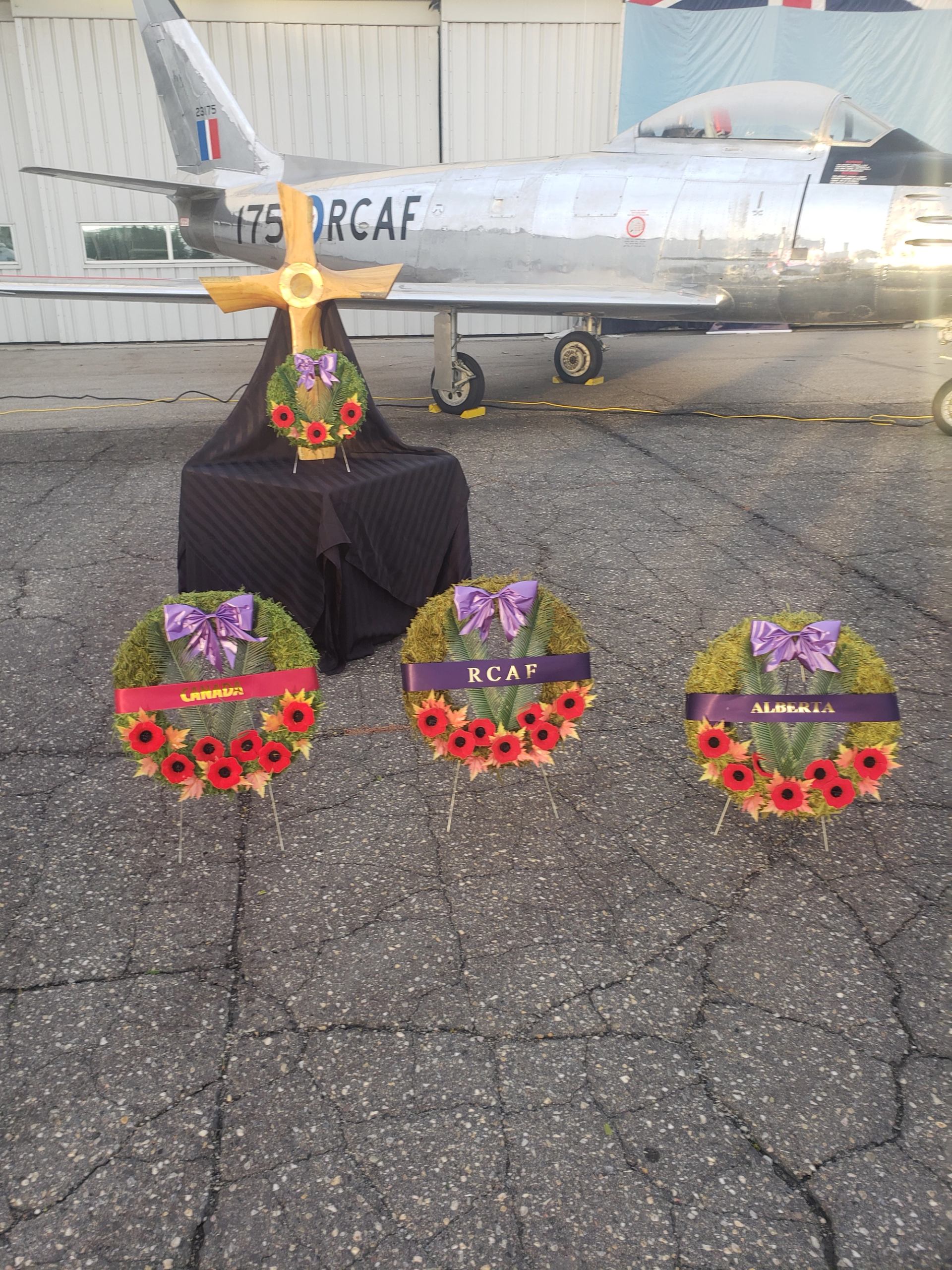 Three wreaths with poppies and a cross displayed in front of a vintage aircraft.