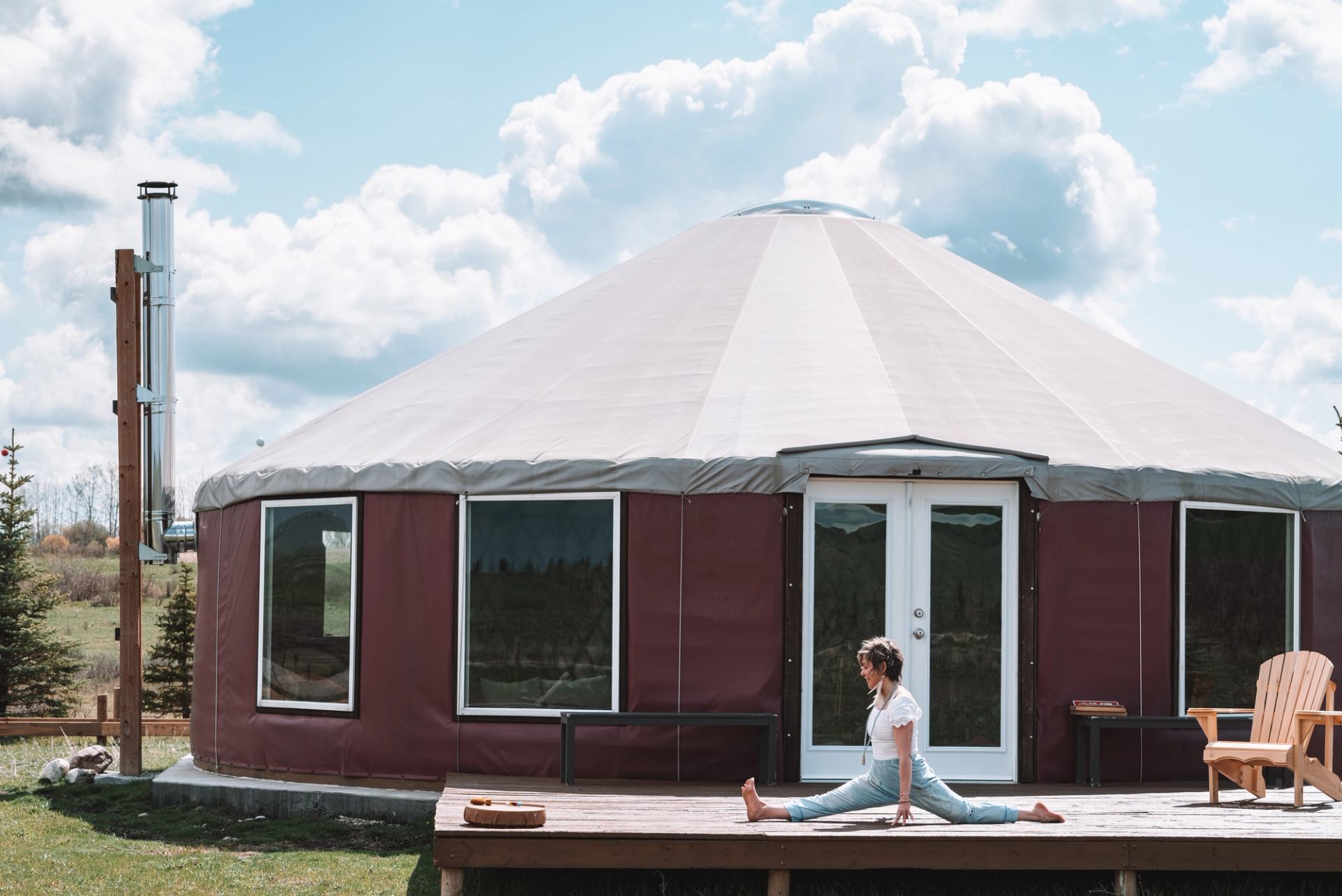 Person performs the splits on a wooden deck outside a round yurt.