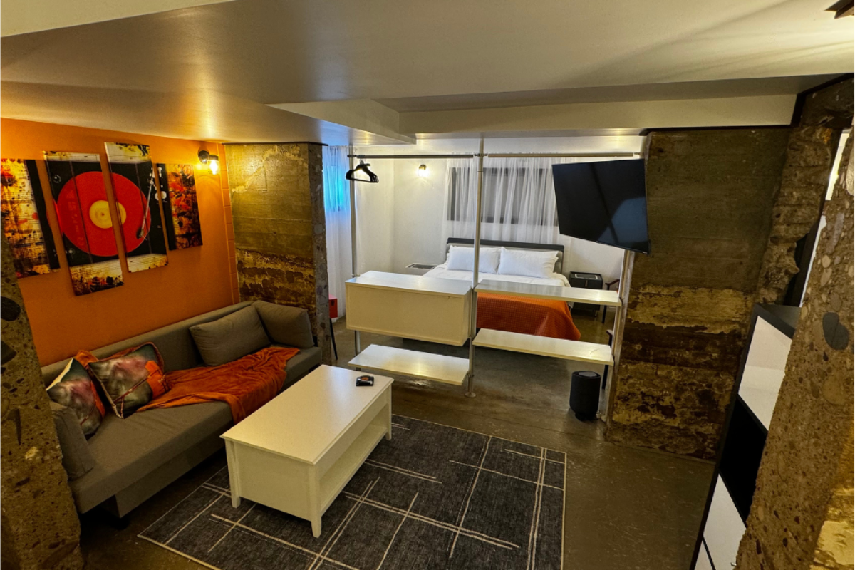 Open-concept room with grey sofa, white coffee table, bed and orange accents.