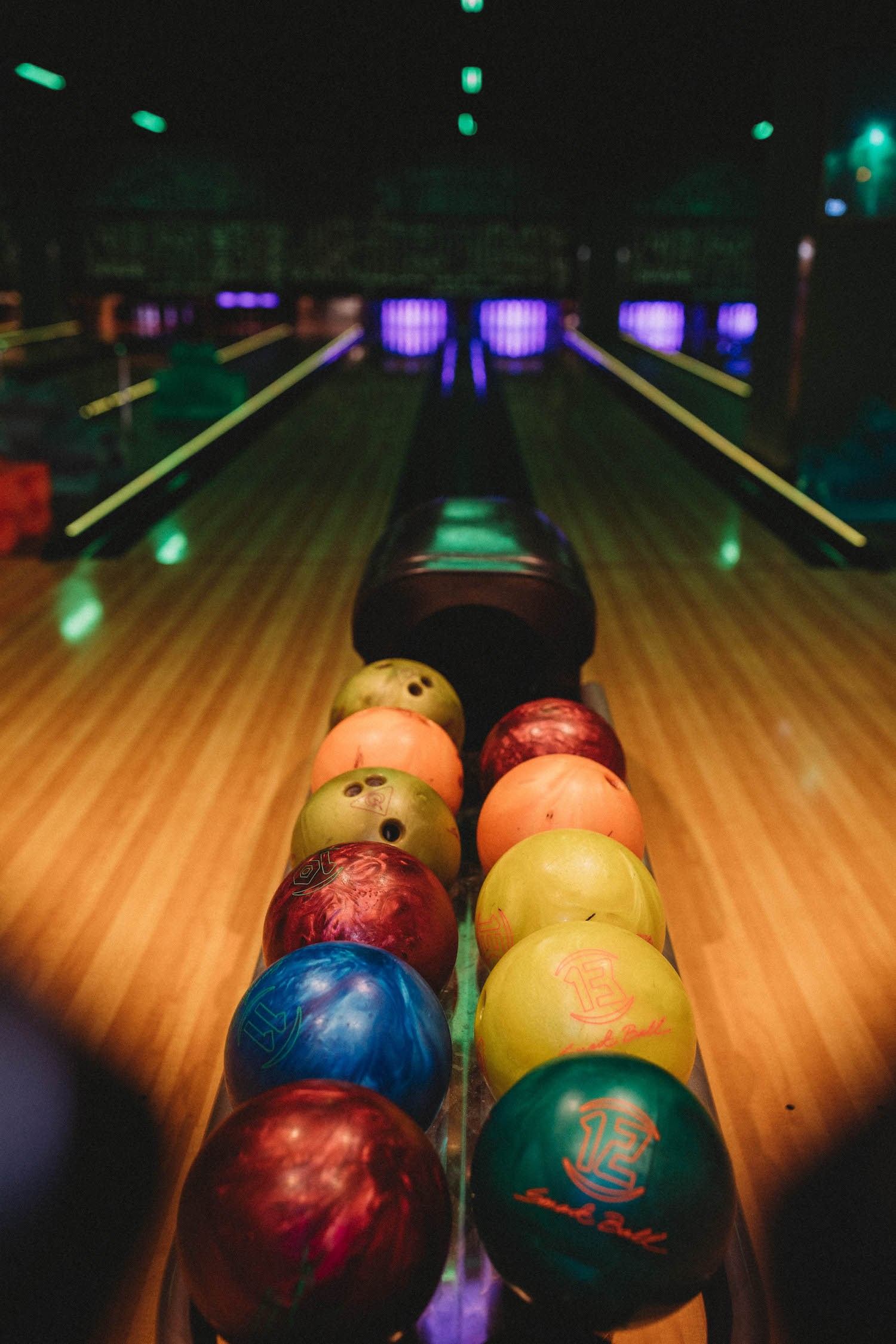 Bowling lane with brightly colored bowling balls and glowing pin decks in the background.