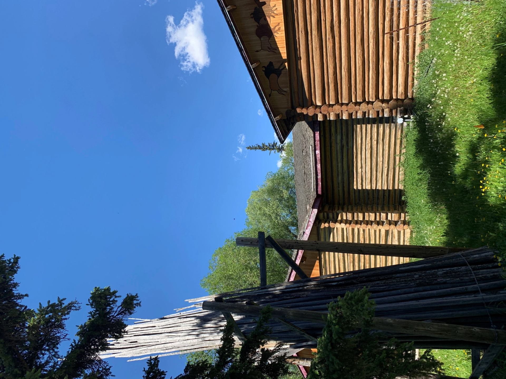 Wooden building wall with carved silhouettes and rope, framed by blue sky and trees.