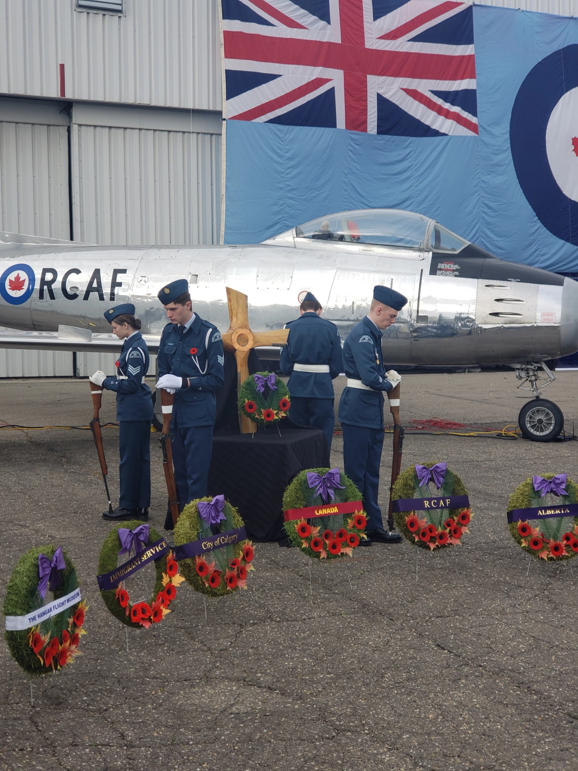 Uniformed individuals placing wreaths in front of a vintage aircraft and flags.