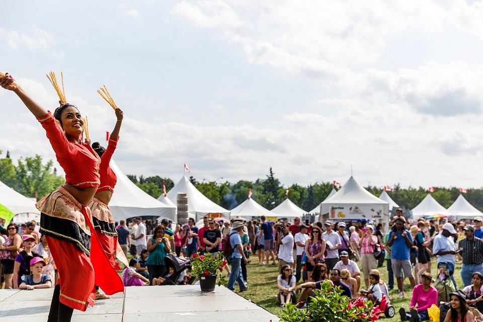 Festival performers in traditional dress dance at crowded outdoor event near white tents.