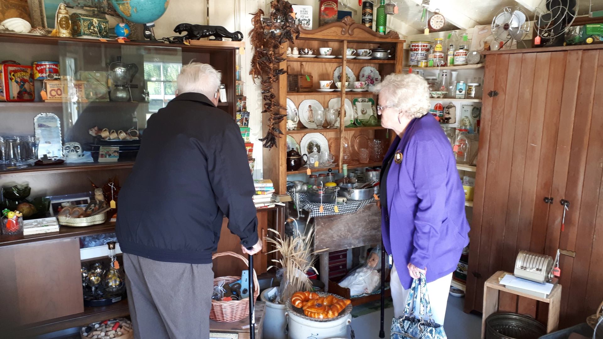 Two people browsing antiques in a cozy shop filled with vintage collectibles.