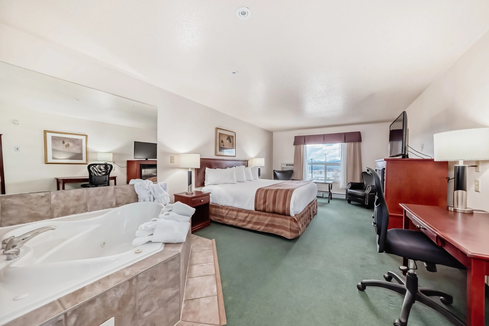 Spacious hotel room with king bed, desk, TV, and in-room whirlpool tub at Grande Cache Inn.