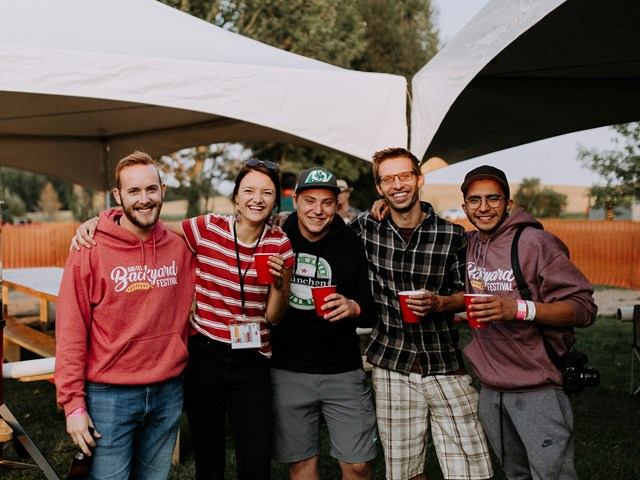 Group of festival attendees under white canopy tents holding drinks and smiling.