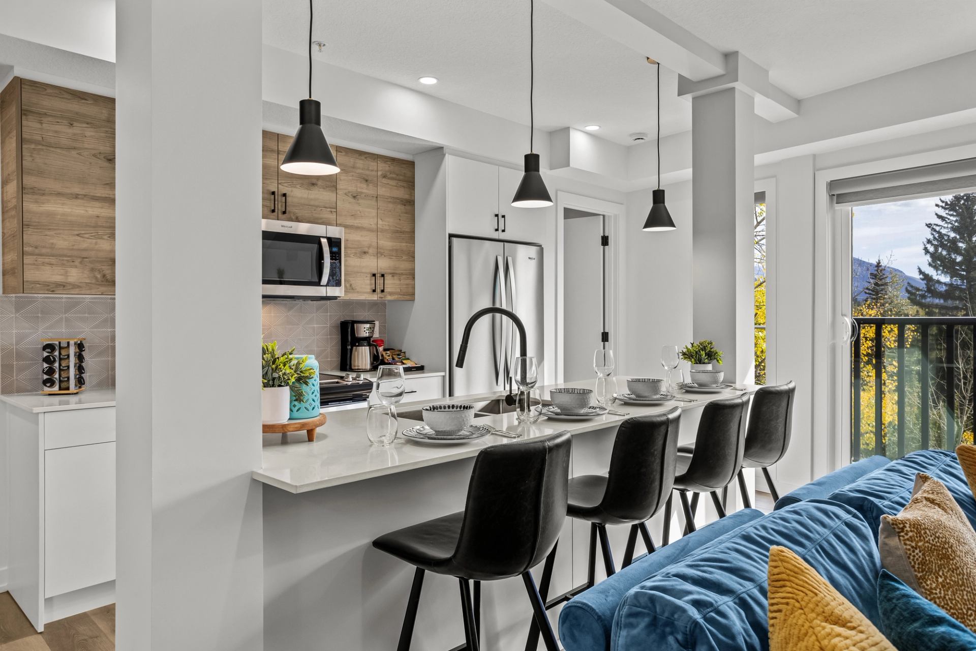 Modern kitchen with island seating, pendant lights and balcony view of trees and mountains.