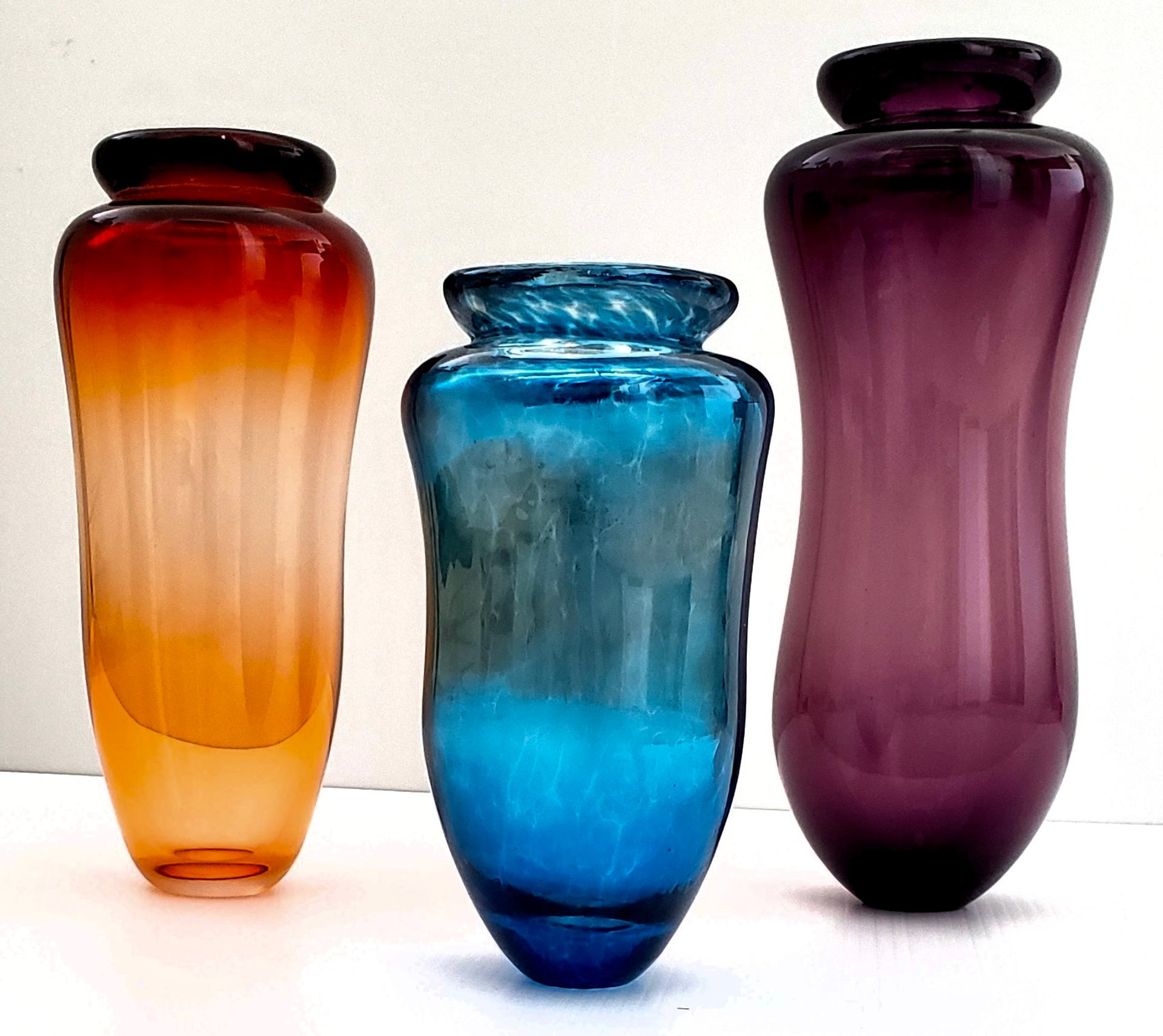 Orange, blue and purple glass vases stand against a white background.