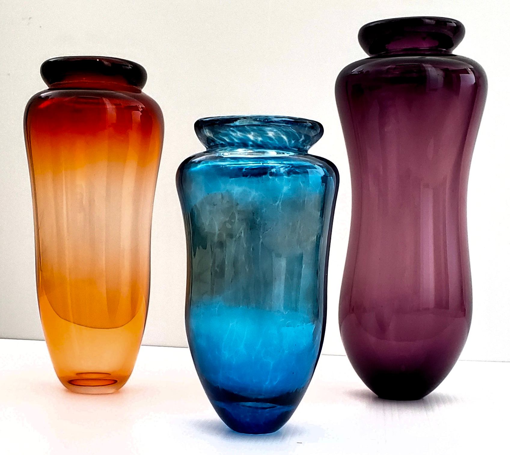 Orange, blue and purple glass vases stand against a white background.