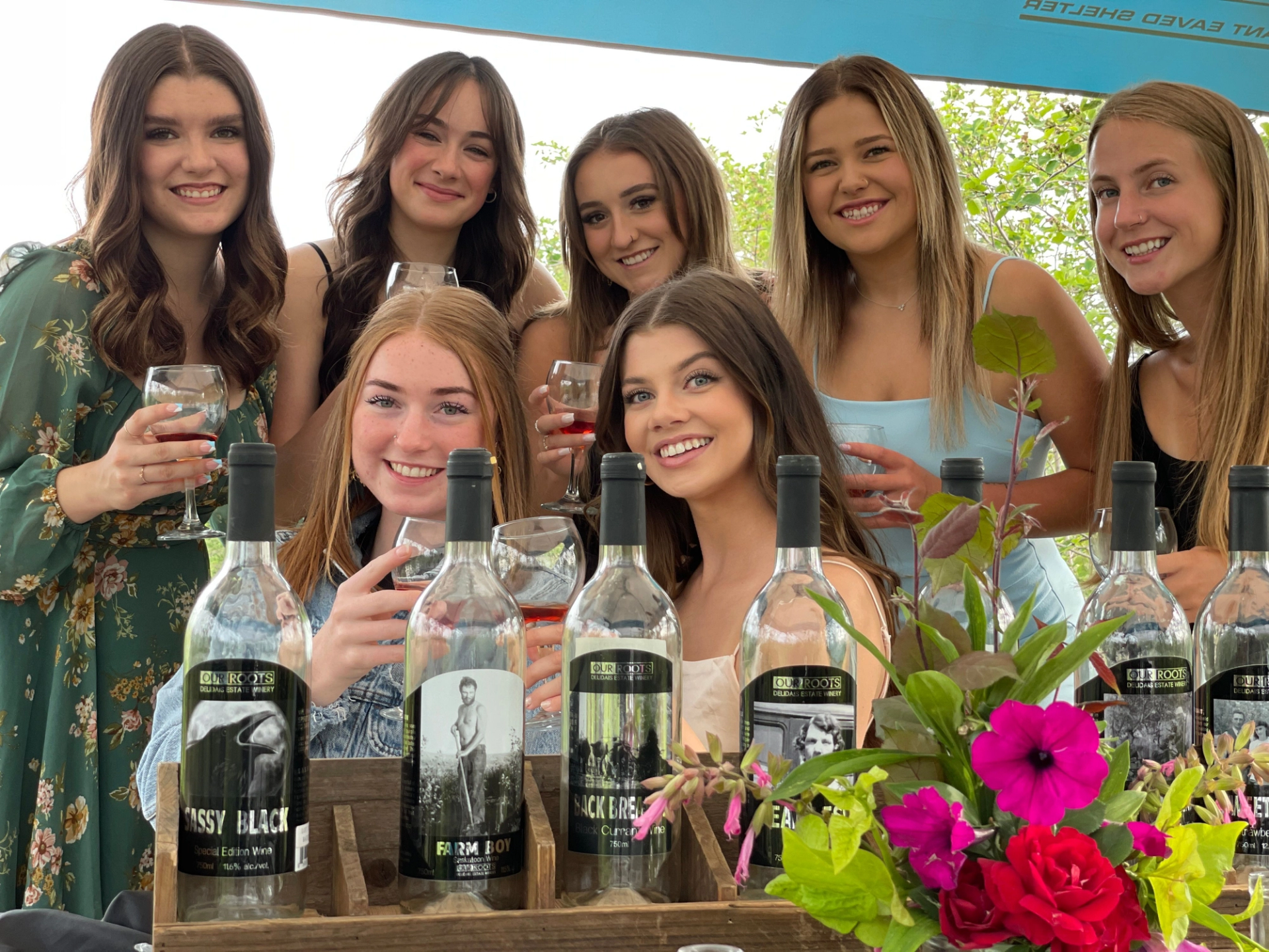Group of people holding wine glasses behind display of wine bottles and flowers.
