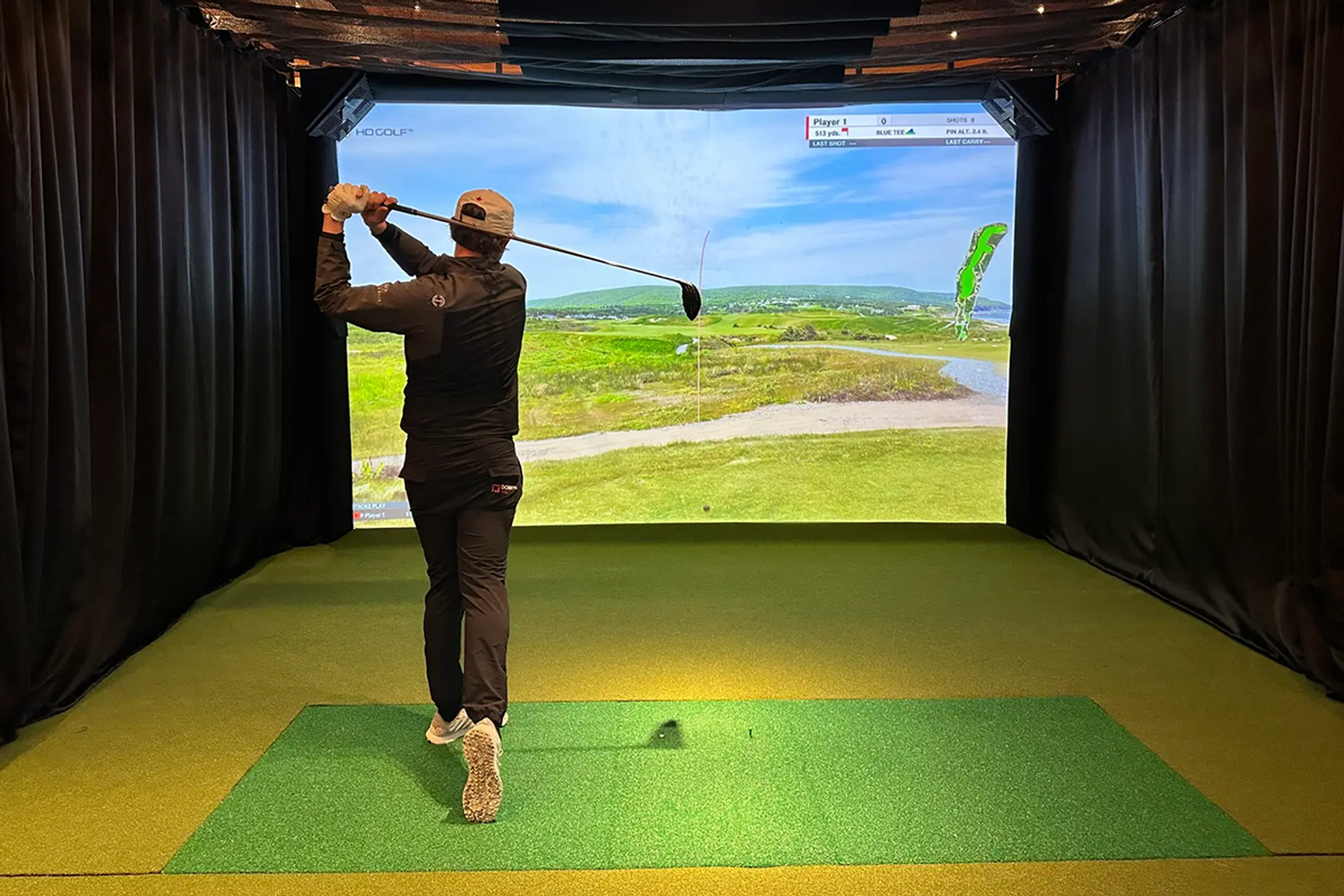 Golfer swinging club in front of a large golf simulator screen.
