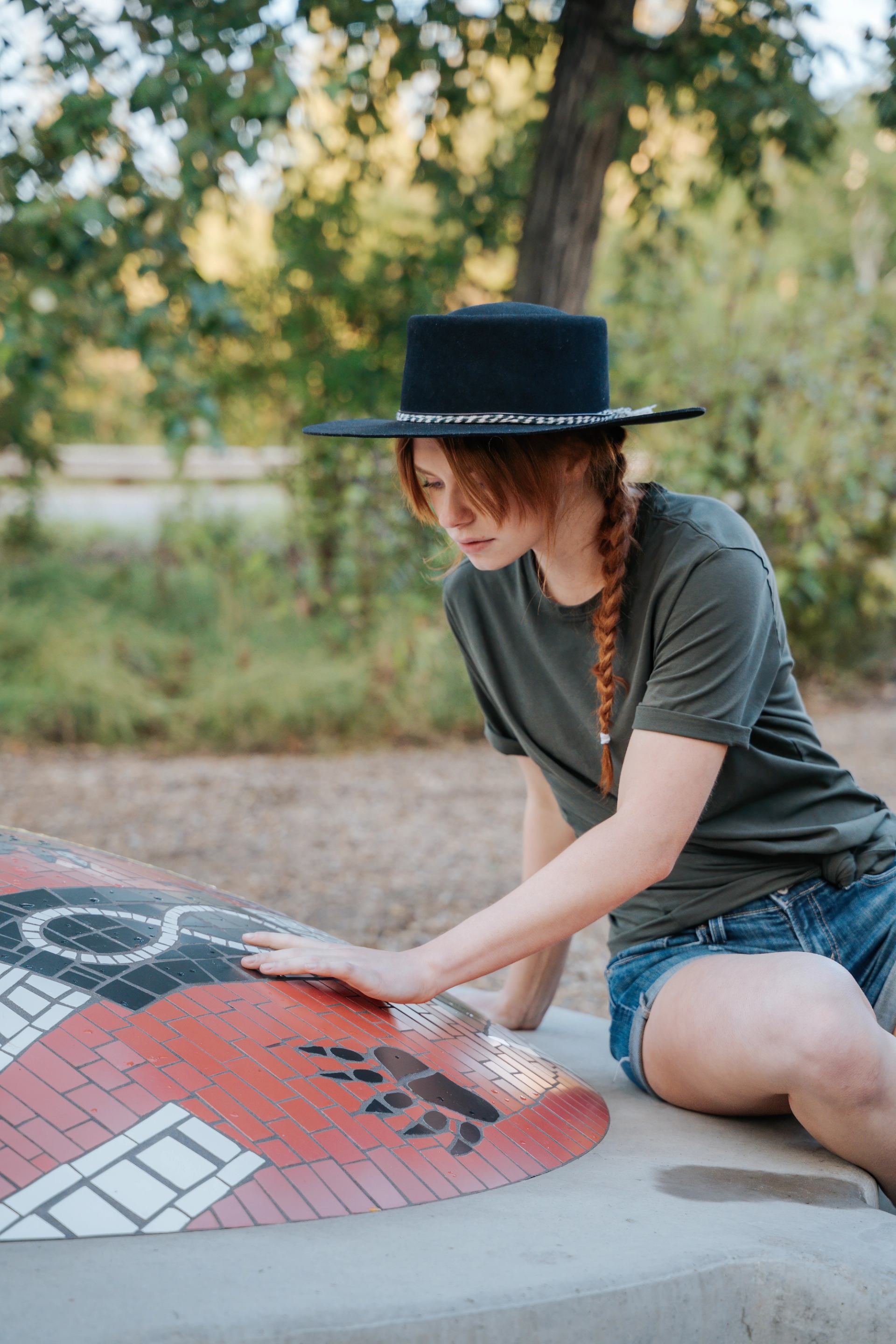 A woman sits beside colourful artwork while tracing out the infinity symbol of the Métis flag.