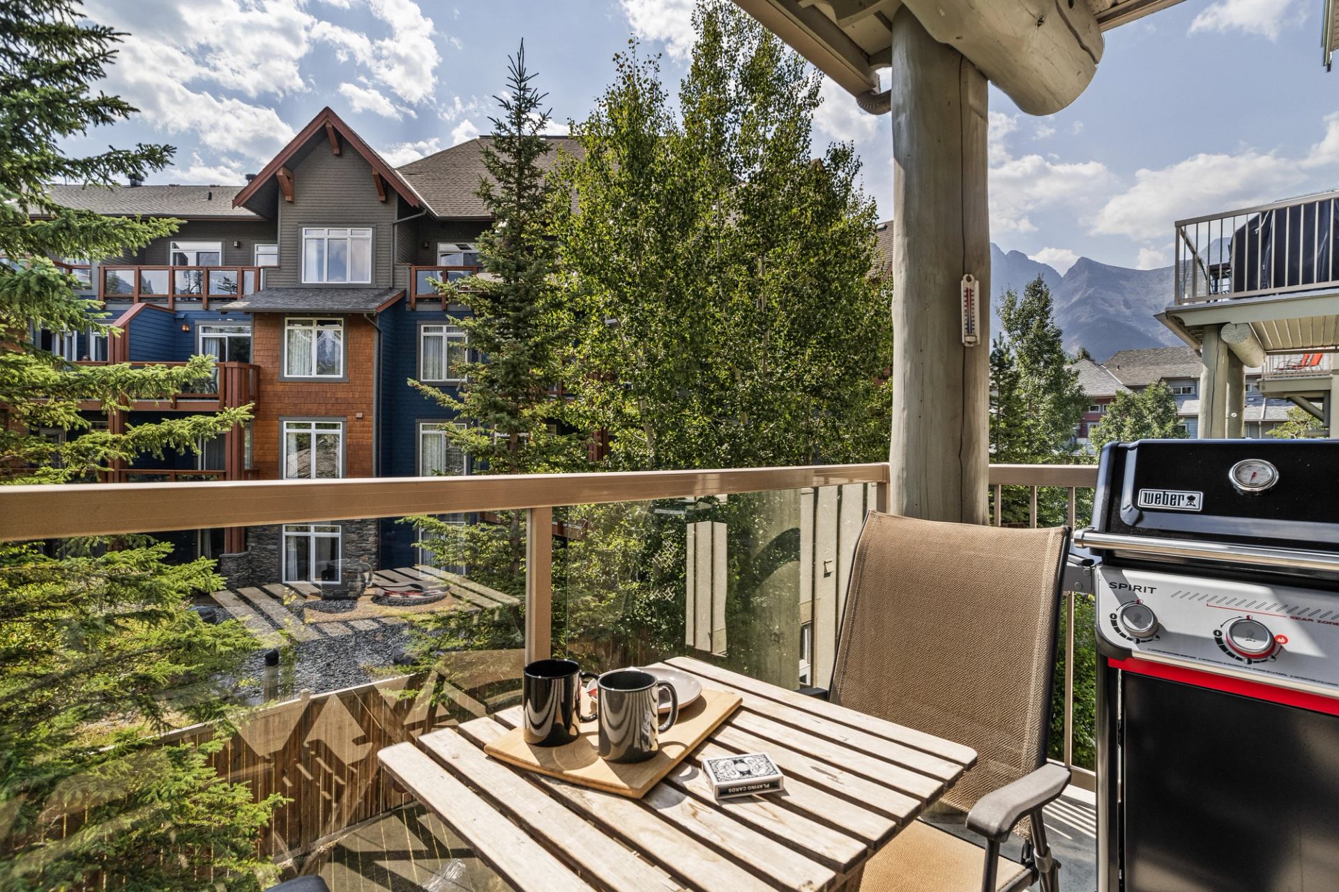 Balcony table with mugs and barbecue overlooks trees, residences and distant mountains.