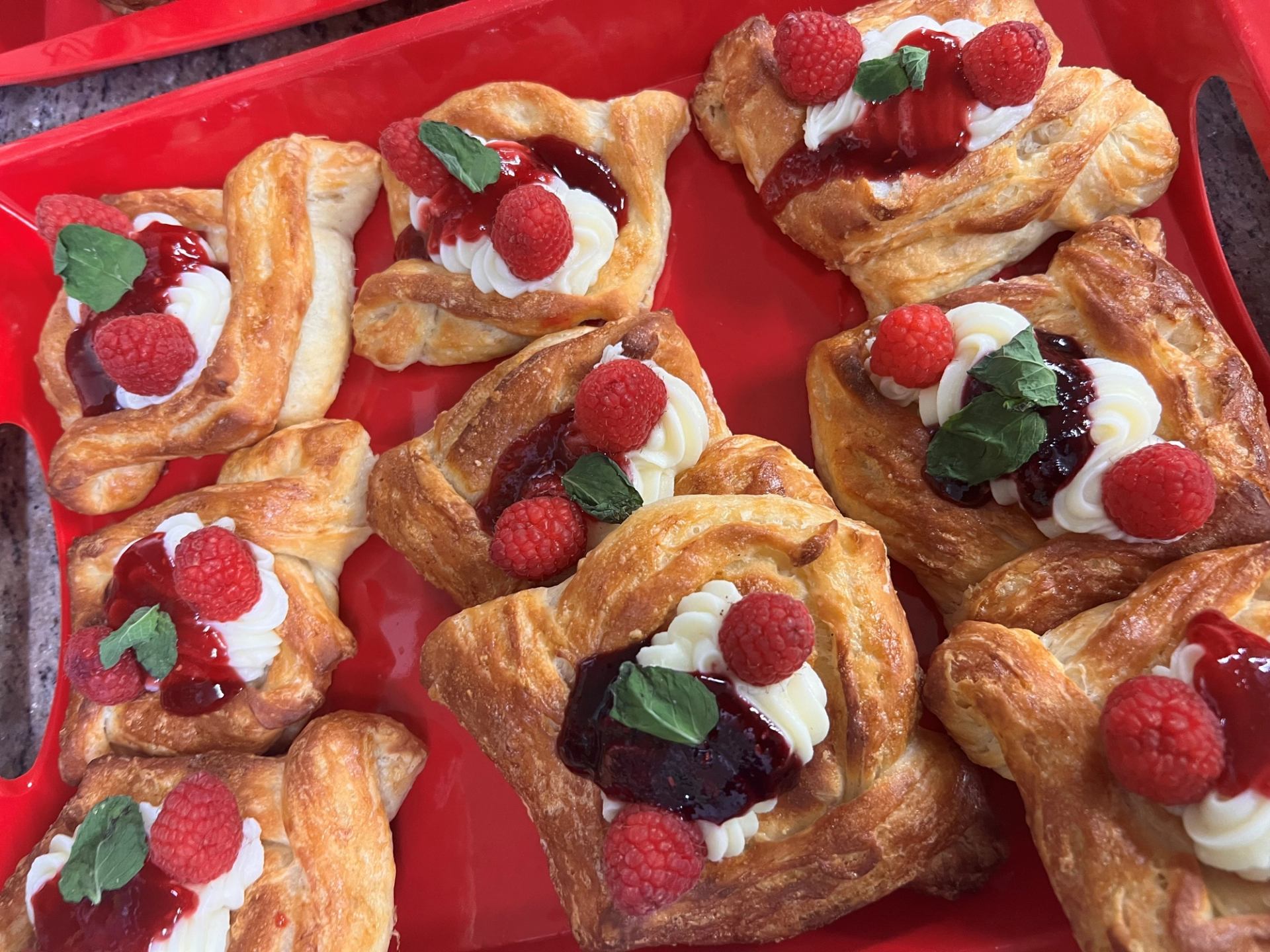 Pastry tarts on red tray topped with white cream, raspberries, and mint leaves.