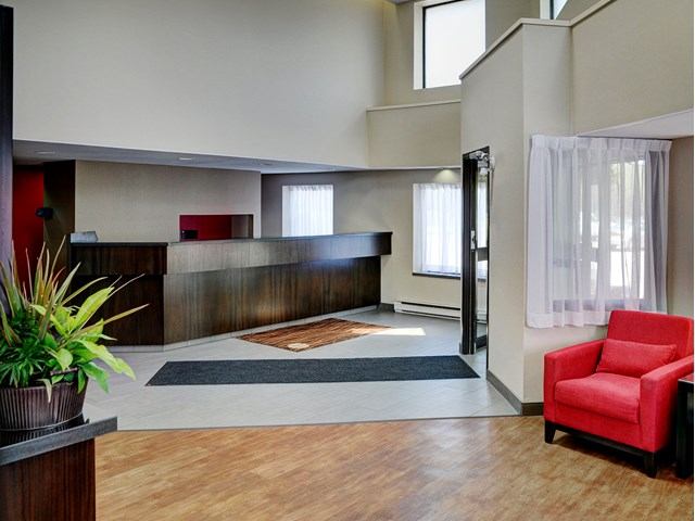 Hotel lobby with front desk, red armchair, potted plant, and bright natural light.