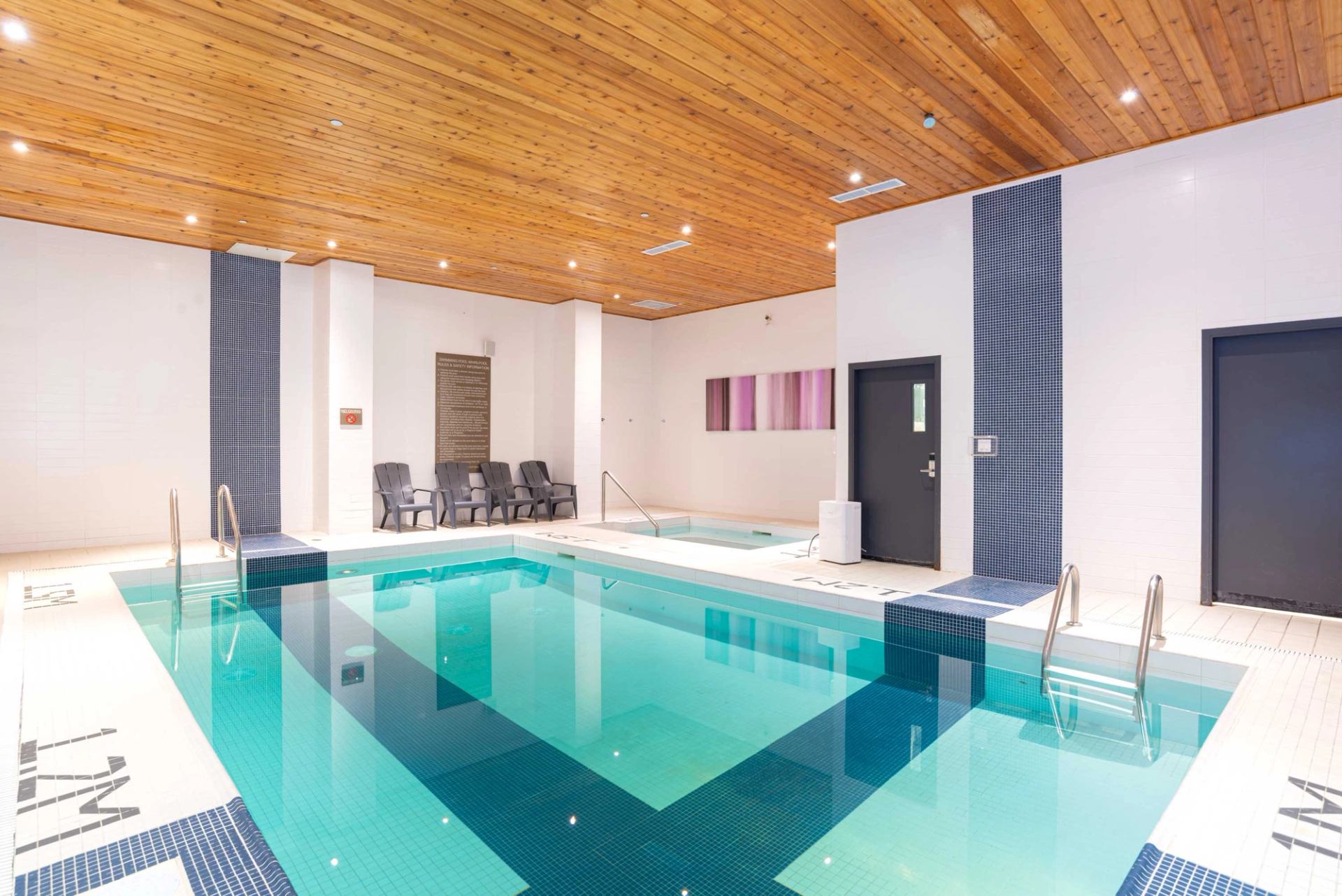Indoor swimming pool with clear water, tiled deck, and wood ceiling.