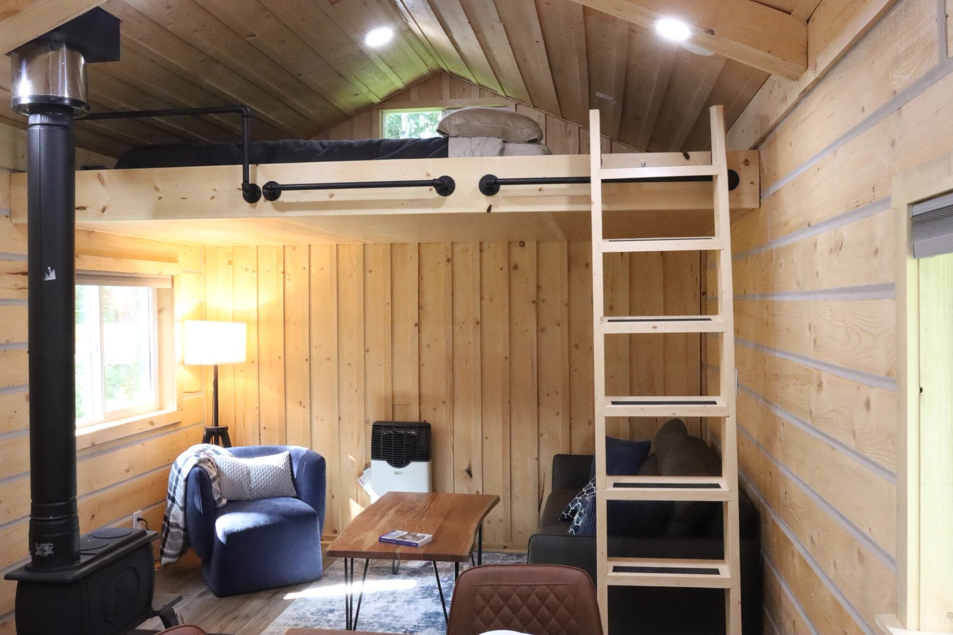 Cozy cabin interior with loft, wood stove, seating area, and warm wooden walls. and ceiling.