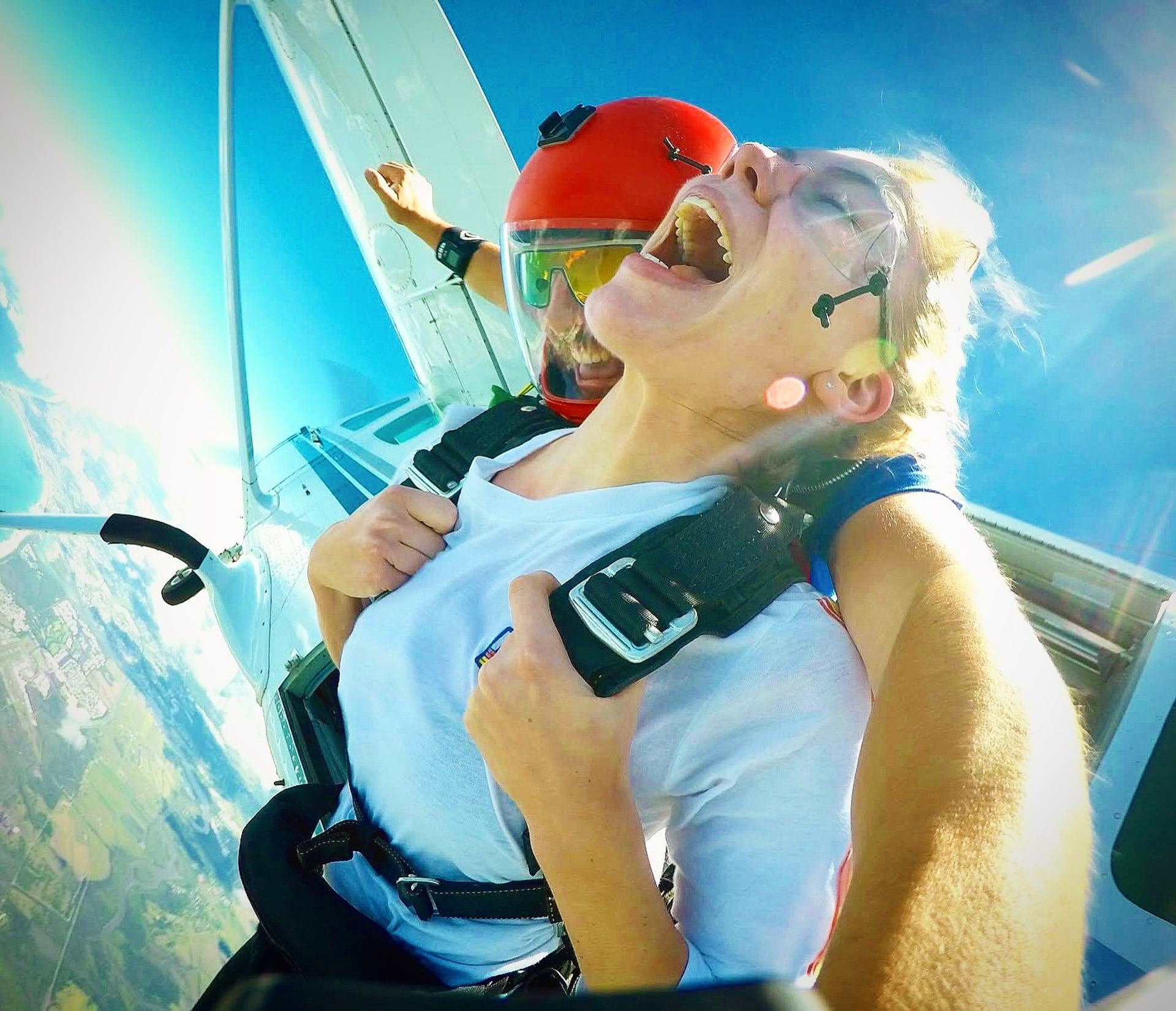 Two people beginning a tandem skydive from a plane high above the landscape.