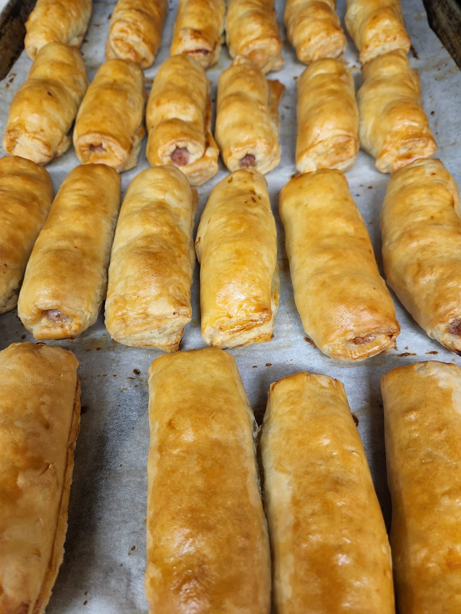 Tray of golden-brown pastry rolls with visible fillings, baked and arranged side by side.