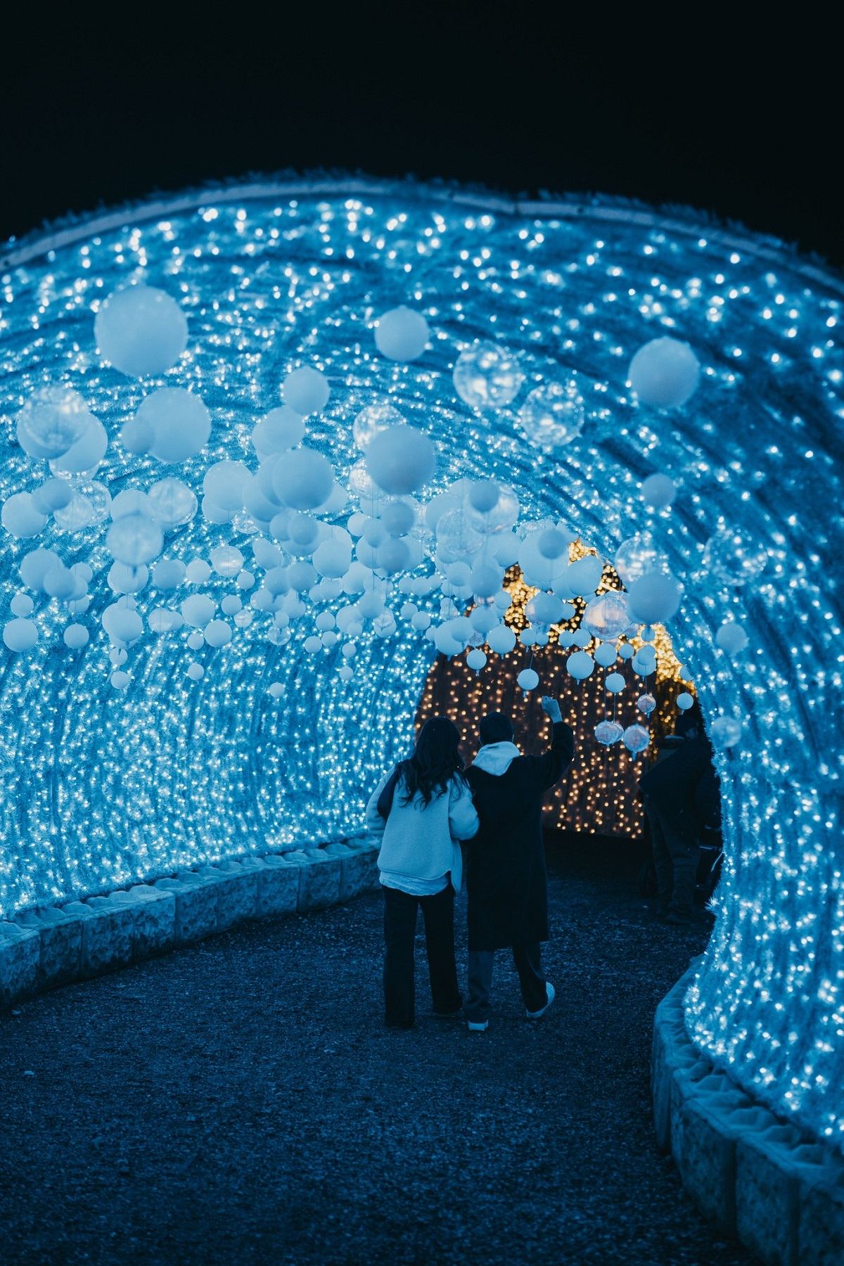 Two people walking through a glowing blue light tunnel at Glow Christmas Festival.