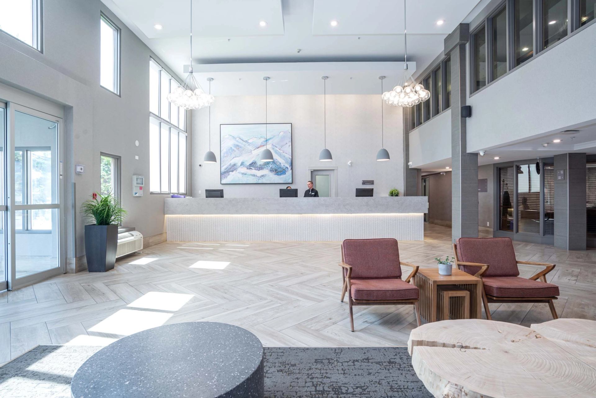 Modern hotel lobby with reception desk, pendant lights, seating area and large windows.