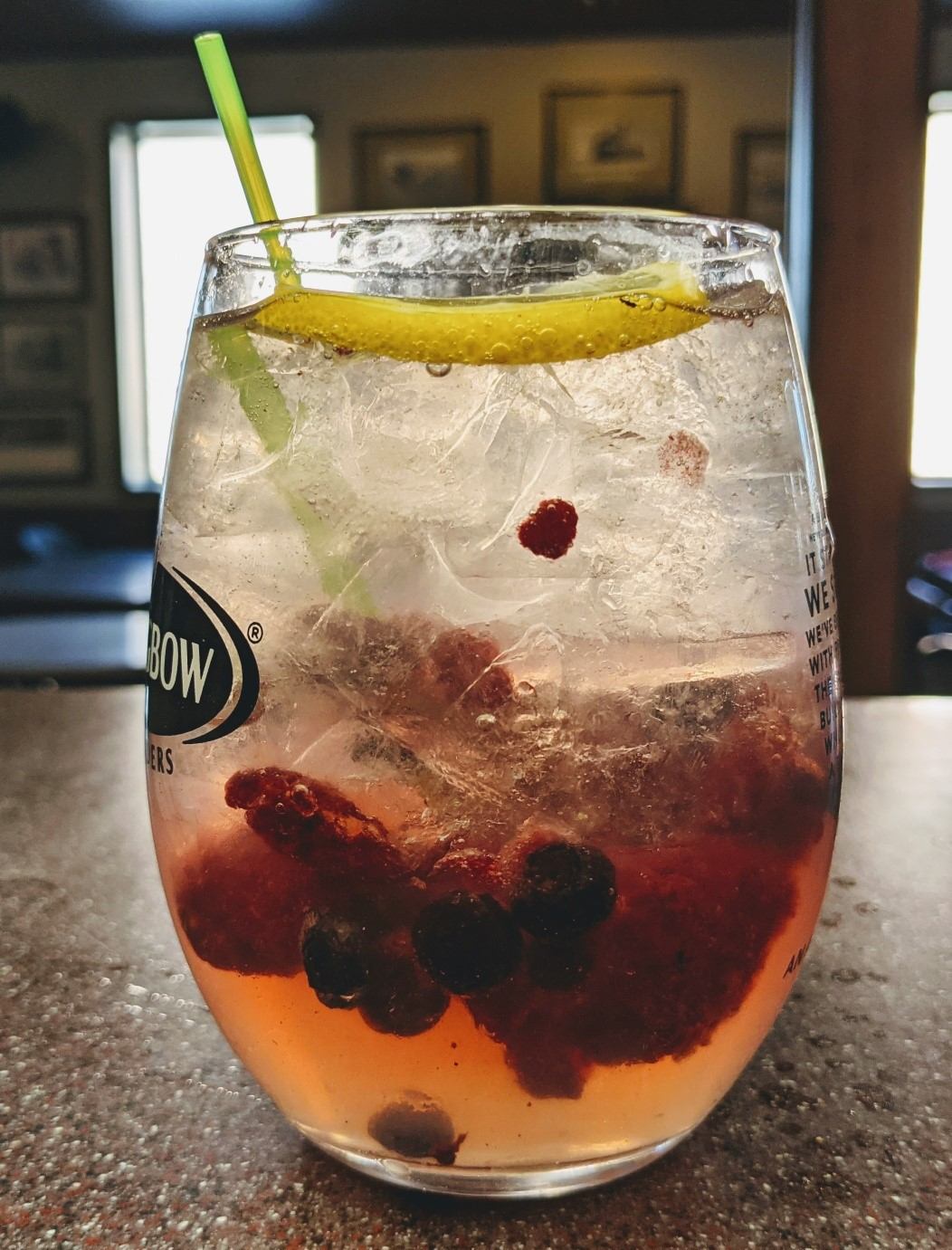 Glass of iced berry drink with lemon slice and green straw on a counter.