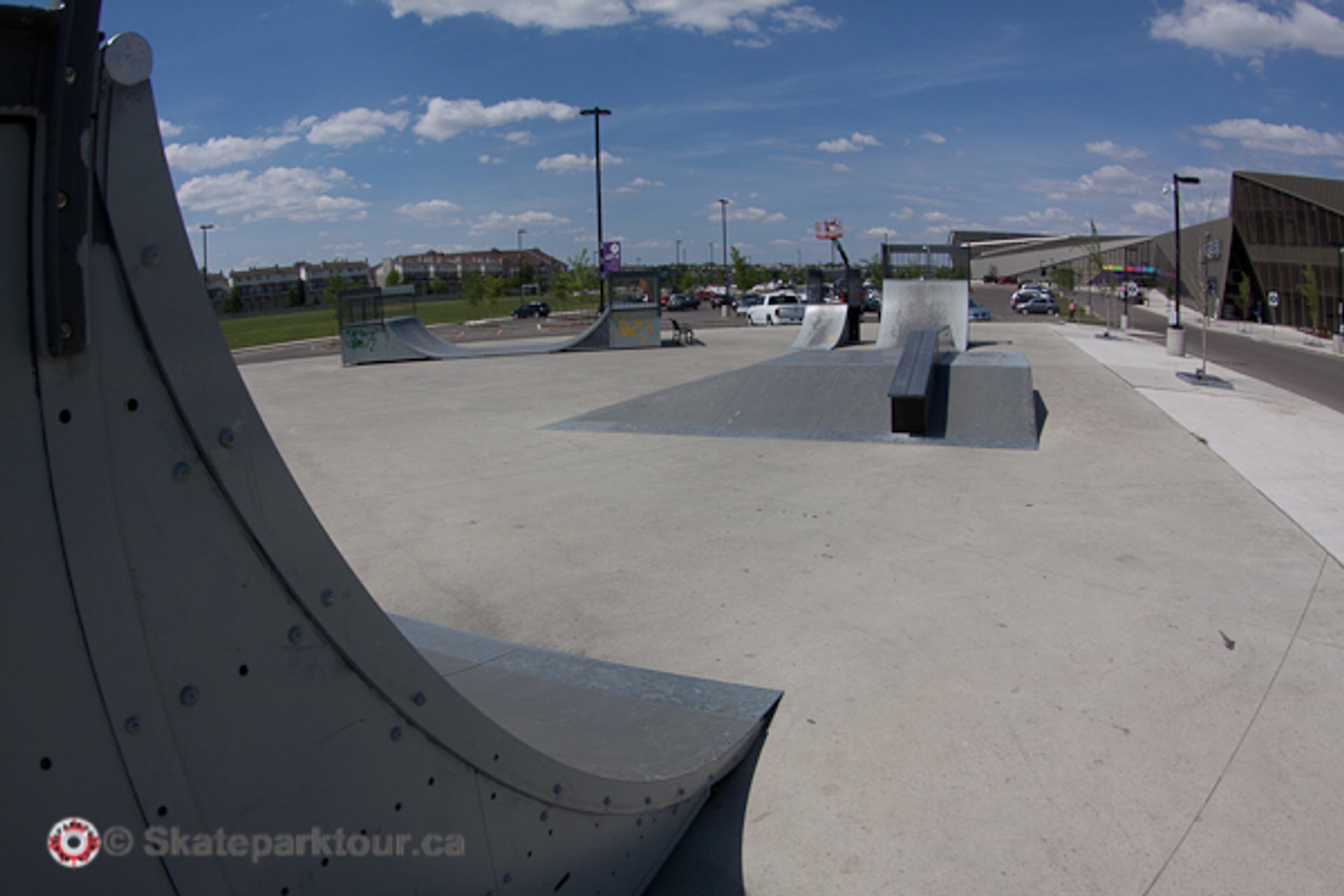Wide concrete skatepark featuring ramps, ledges, and riding elements beneath a blue sky overhead.