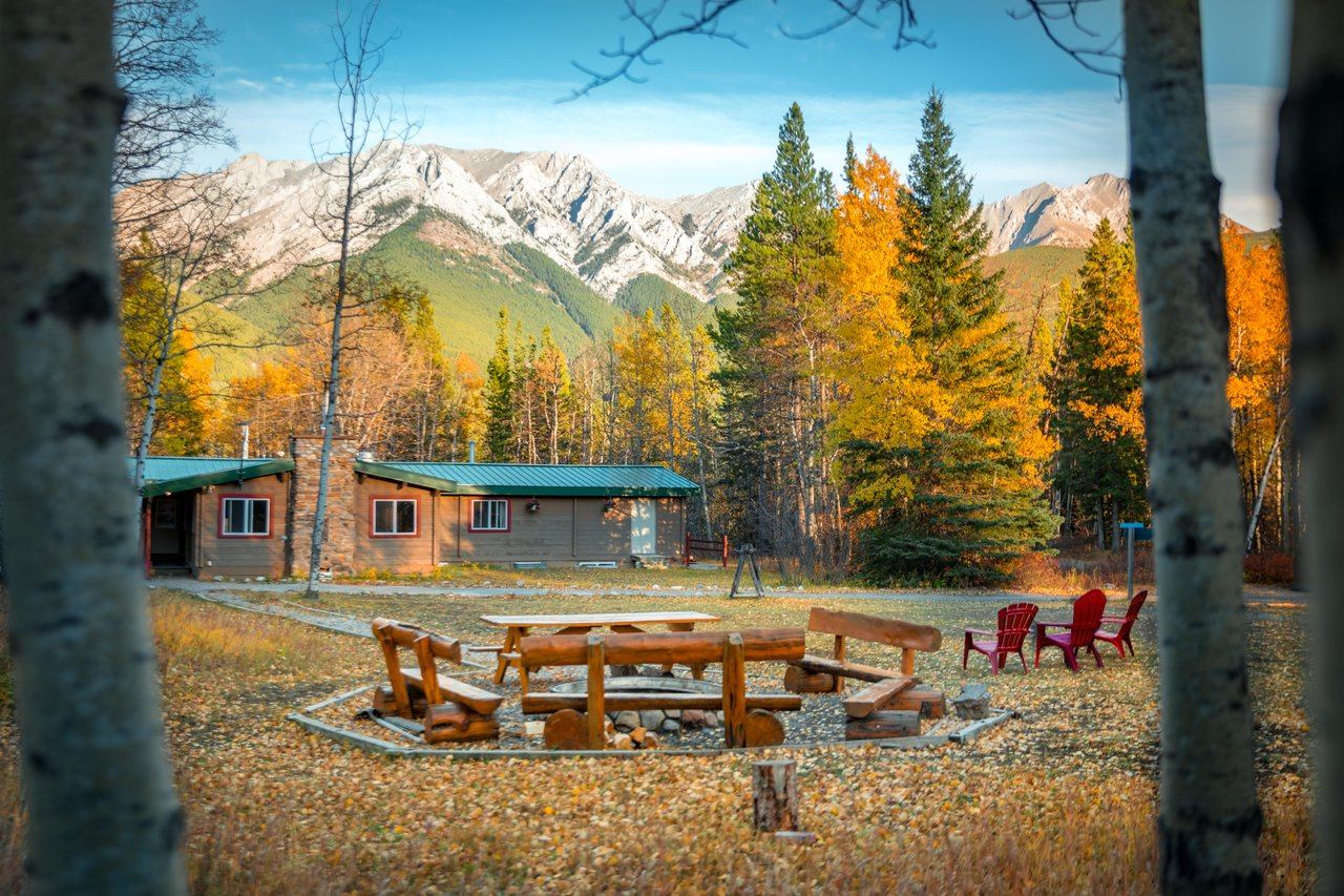 Autumn exterior of HI Kananaskis with wooden cabins, circular fire pit with log benches, red chairs.