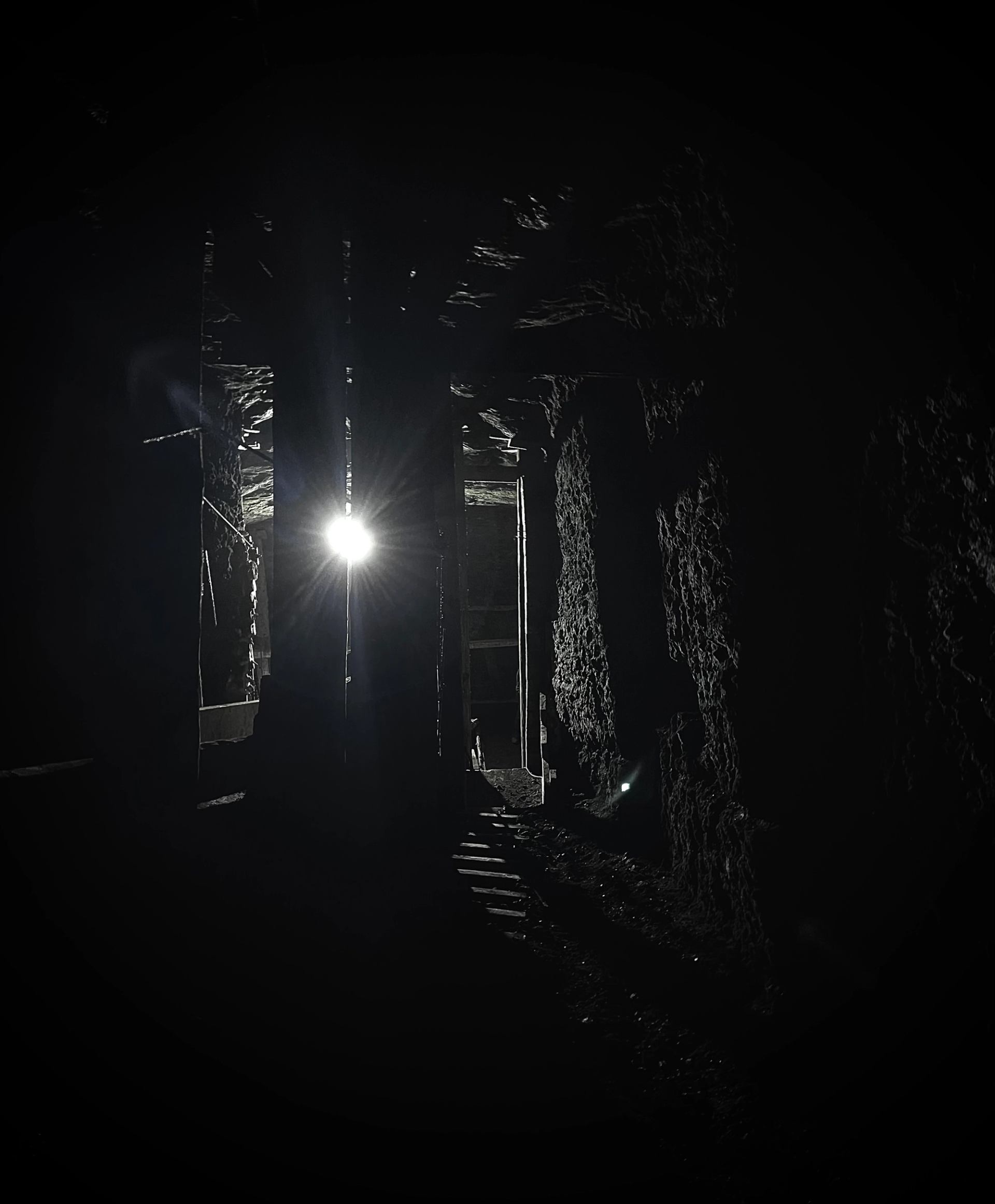 Dim light shining through a narrow, rocky tunnel in Bellevue Underground Mine.