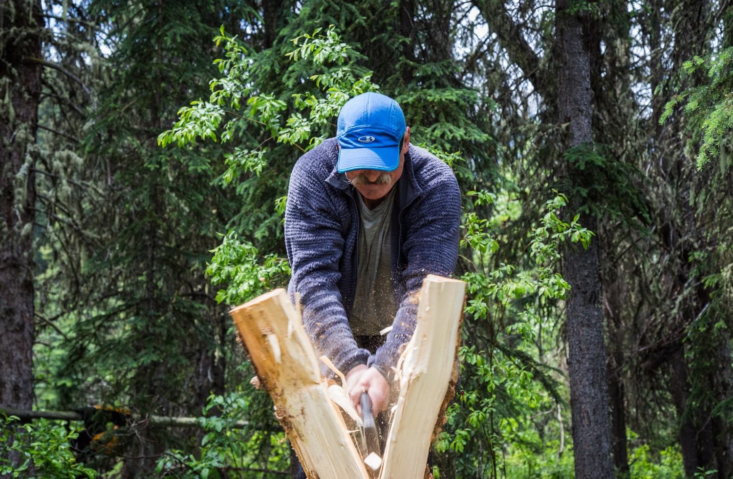 Person splits wood with axe in forest setting at Wild Current.
