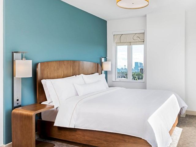Modern bedroom with teal accent wall, white bedding, and city view.