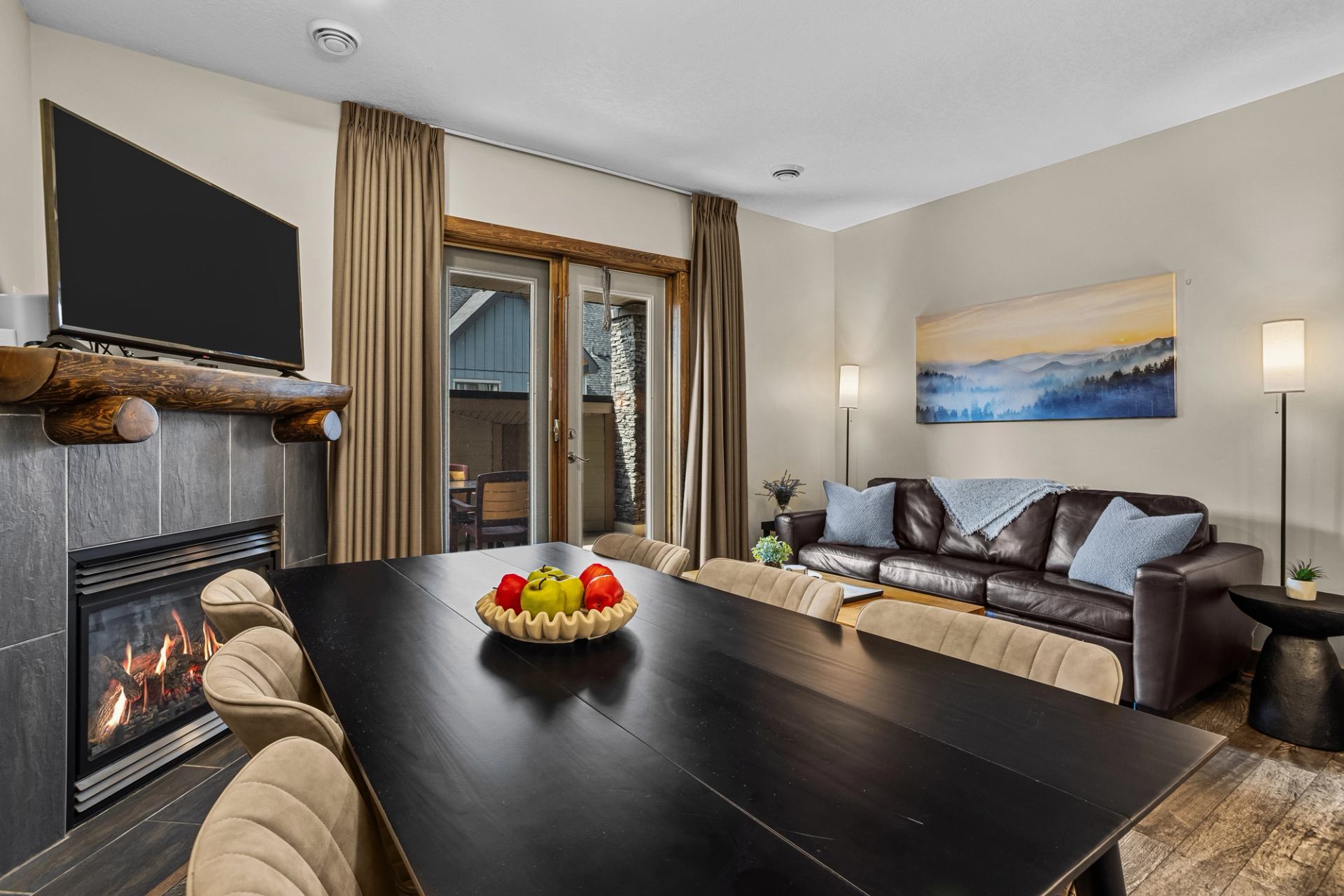 Dining and living area with fireplace, television, dark table and leather sofa.