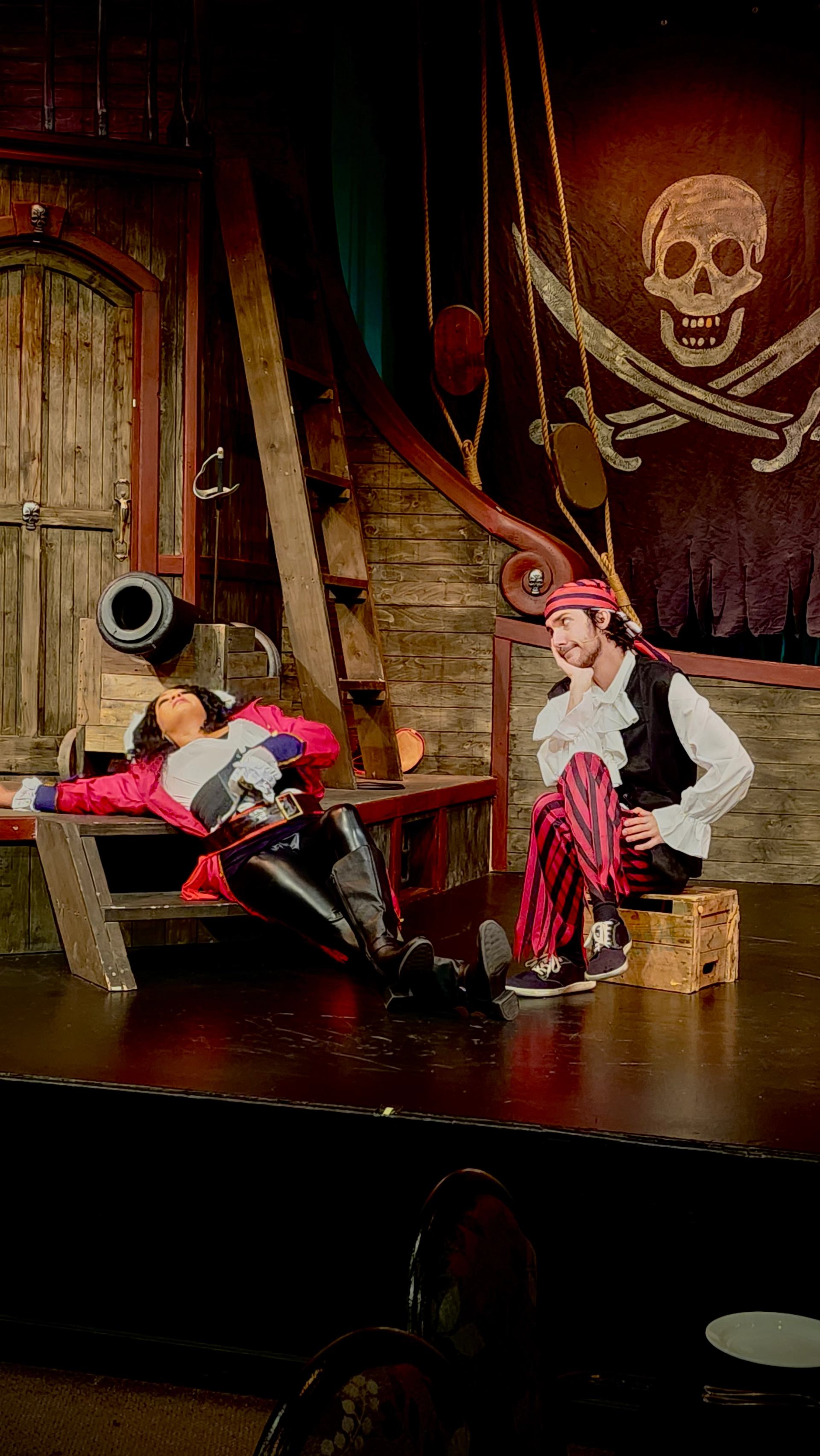 Two performers in pirate costumes act out a humorous scene on a ship‑themed stage.