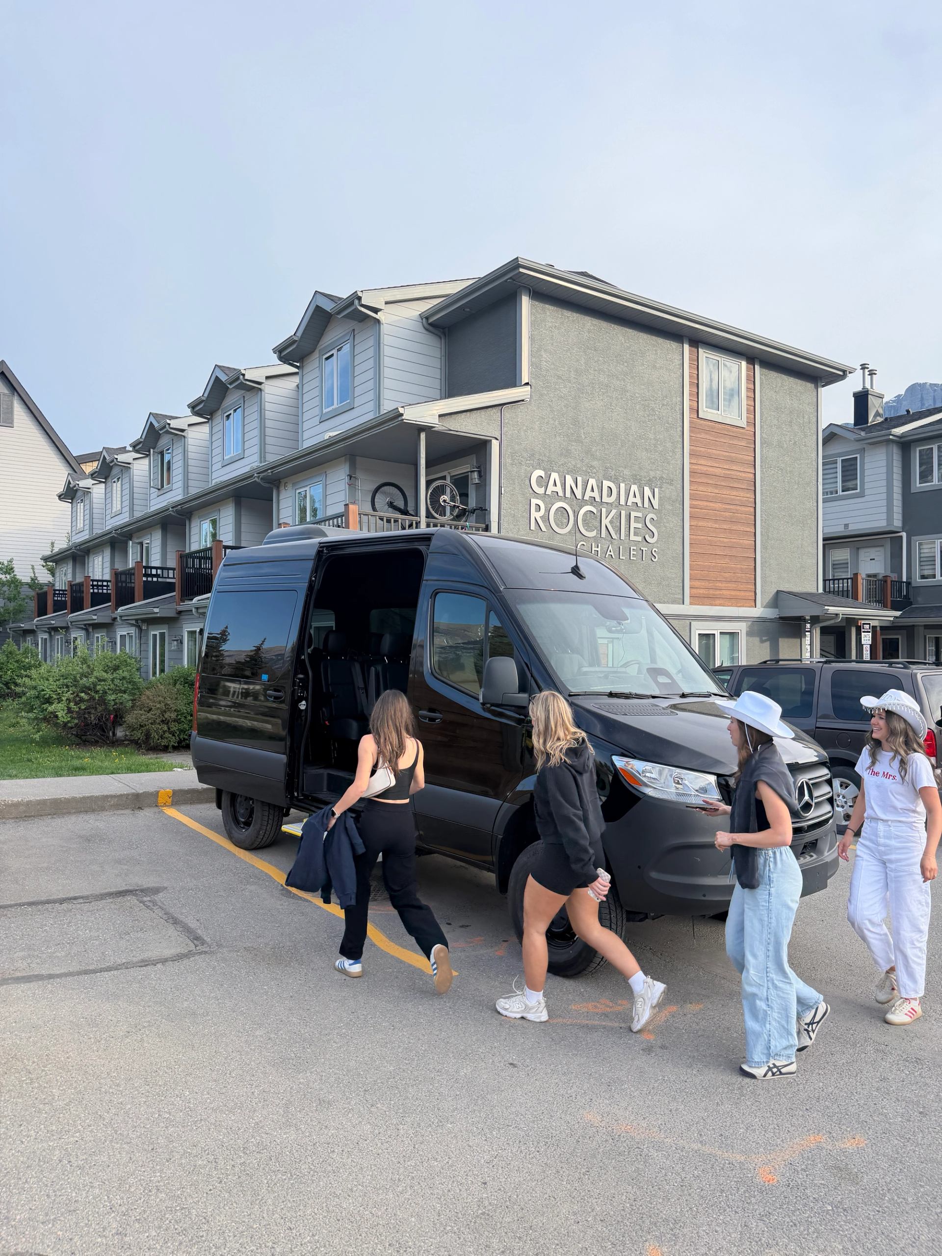 People walking toward a black van parked outside Canadian Rockies Chalets building.
