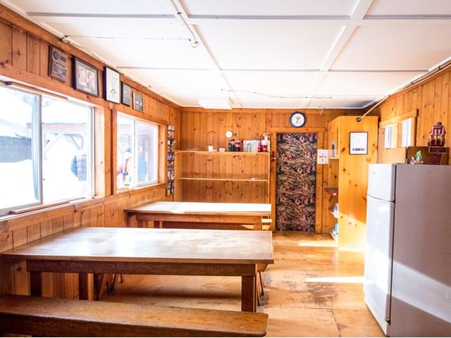 Rustic dining room with wooden tables, benches, and natural light from large windows.
