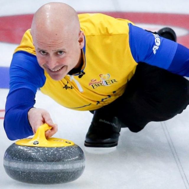 Curler in yellow and blue jersey releases a curling stone on ice.